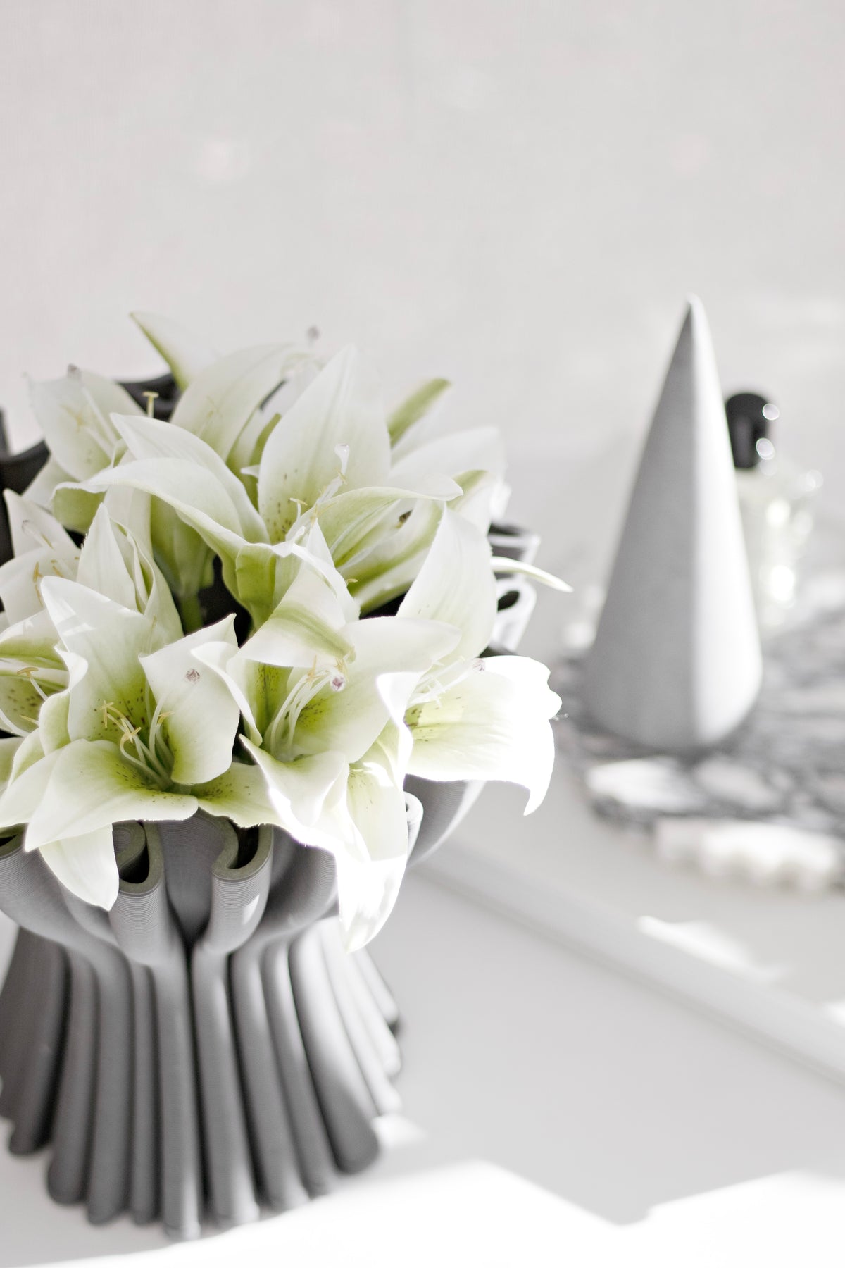 Cream lilies in a grey fluted vase beside a white cone ornament