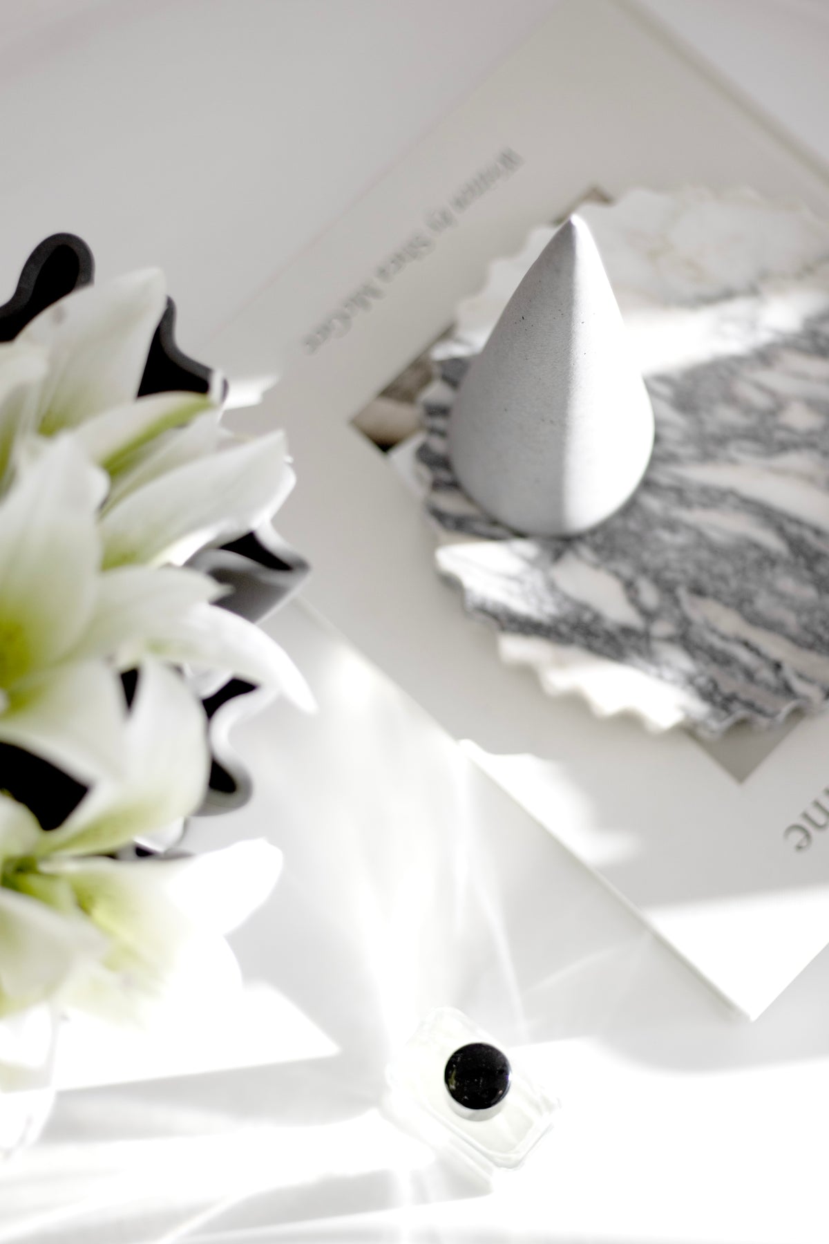 Cream lilies beside an open magazine and a white cone ornament in bright light
