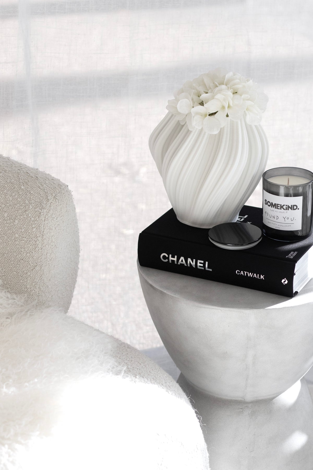 Small white Amelie fluted vase with a white bloom on a plaster plinth beside a candle