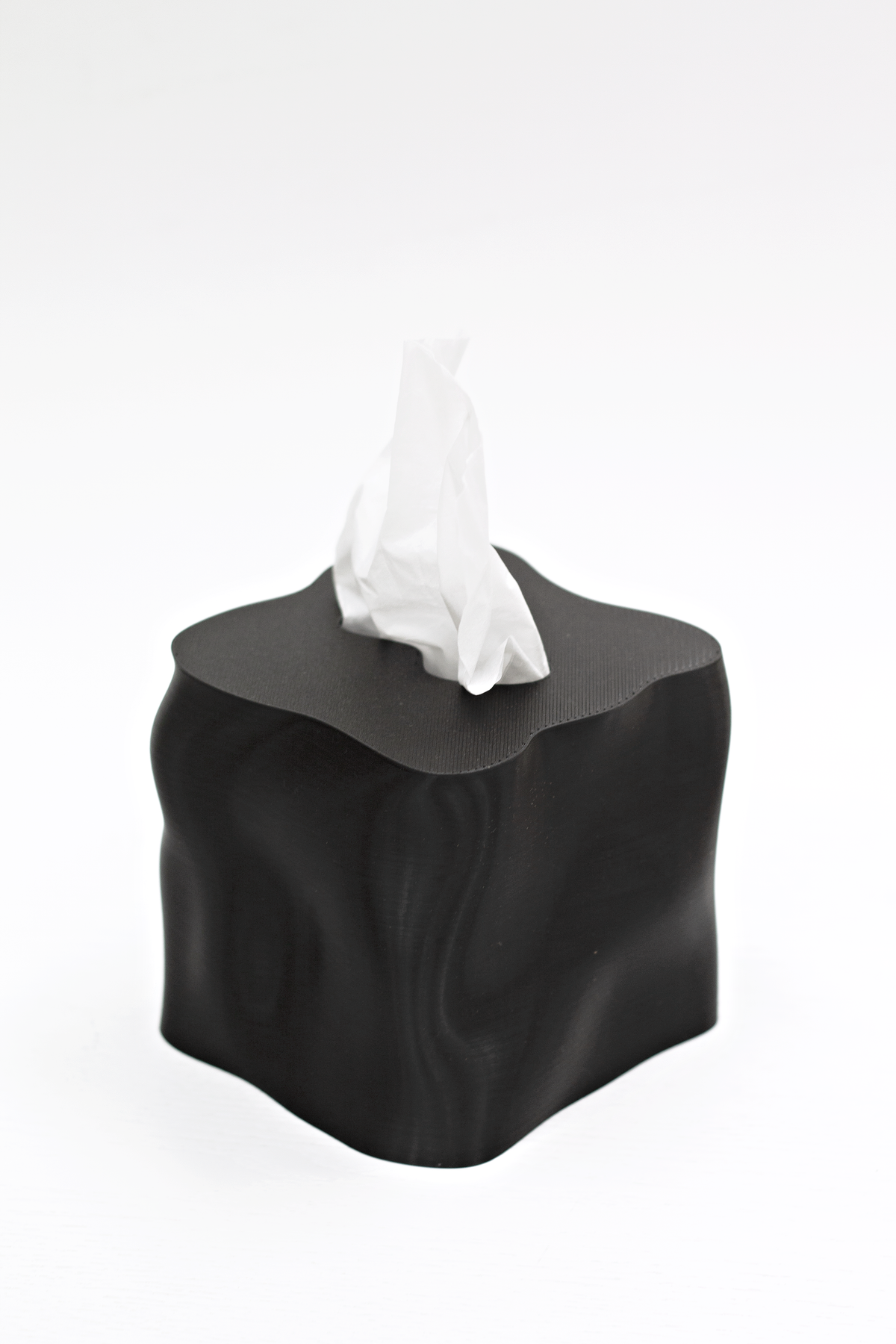 Ebb tissue box cover in black with a tissue drawn up through the shaped opening
