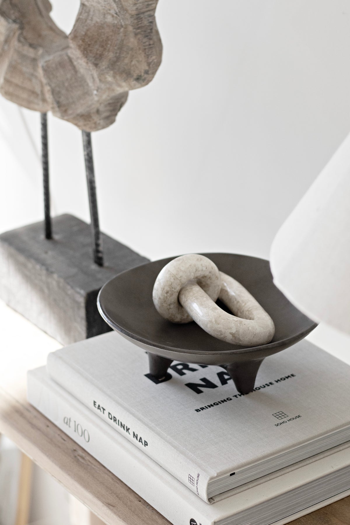 The wooden sculpture at the edge of a console with a dark bowl and a knot on books