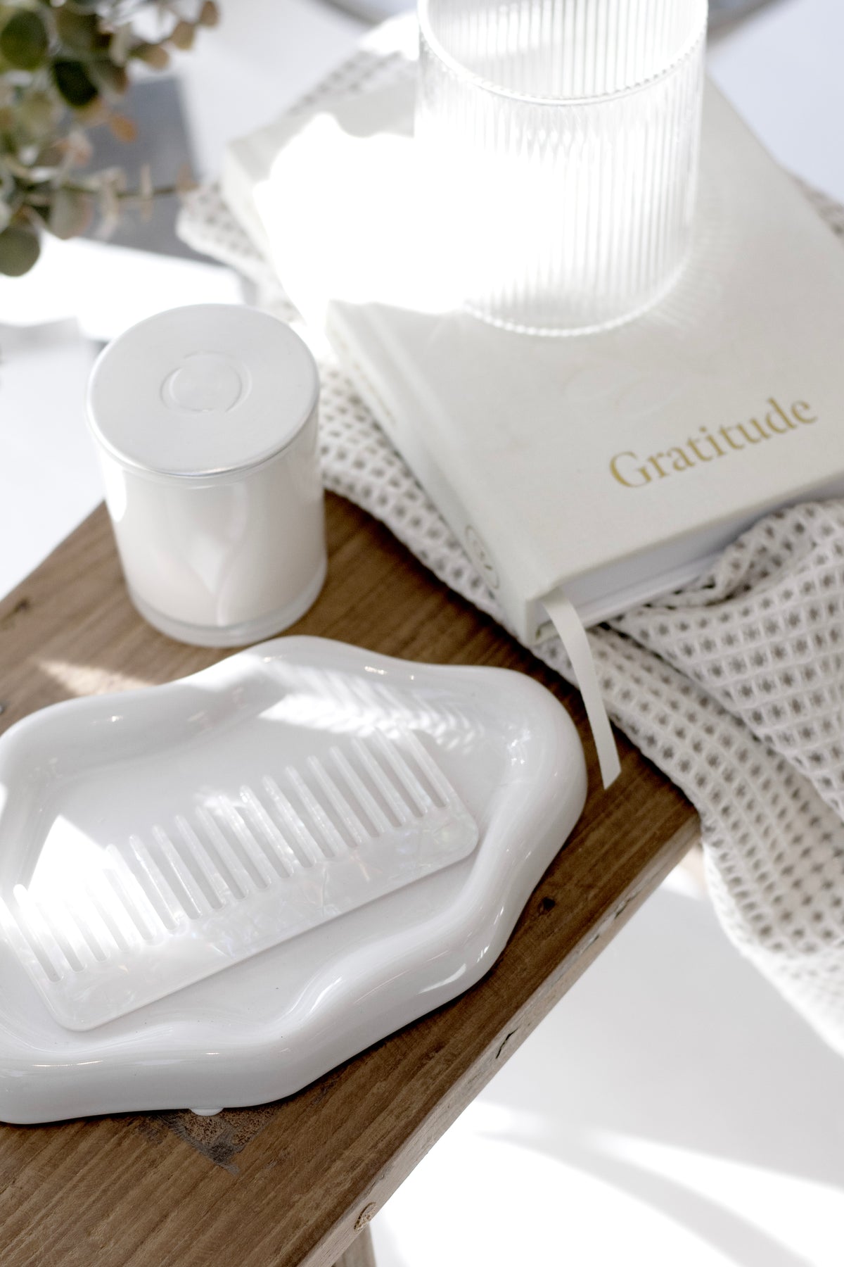 Gratitude journal on a timber bedside with a white candle and wavy ceramic dish