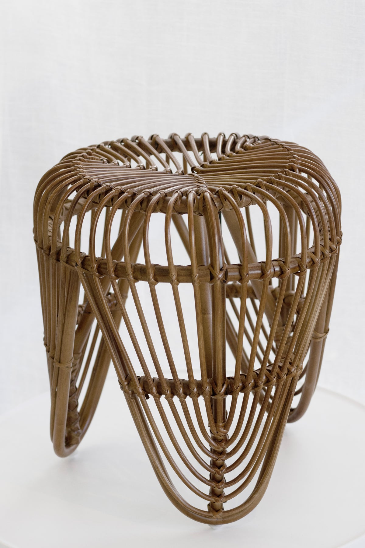 Rattan tulip stool on a plain background, angled to show the woven seat