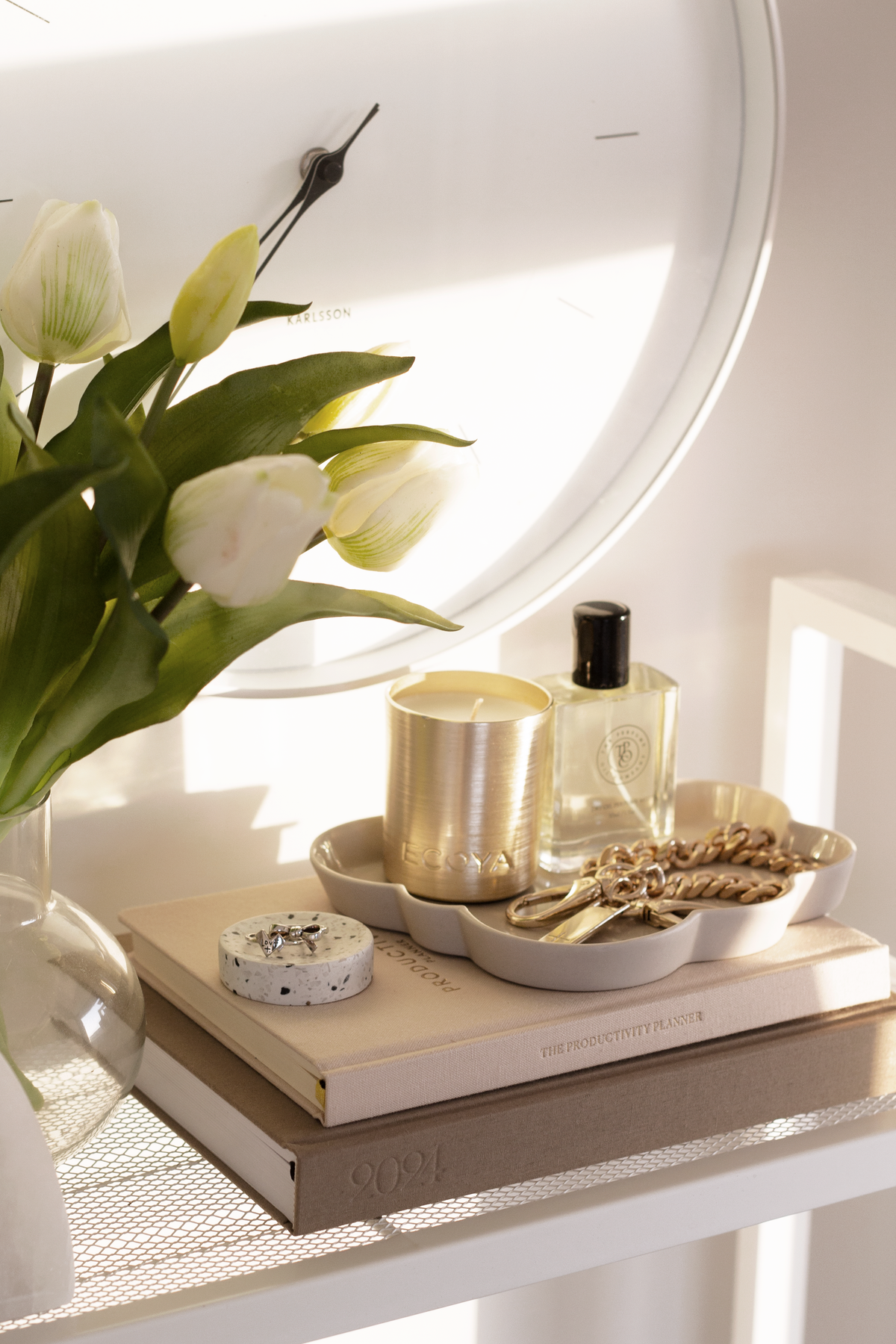 White faux tulips in a glass vase on a dressing table with a scalloped tray, perfume bottle and round mirror