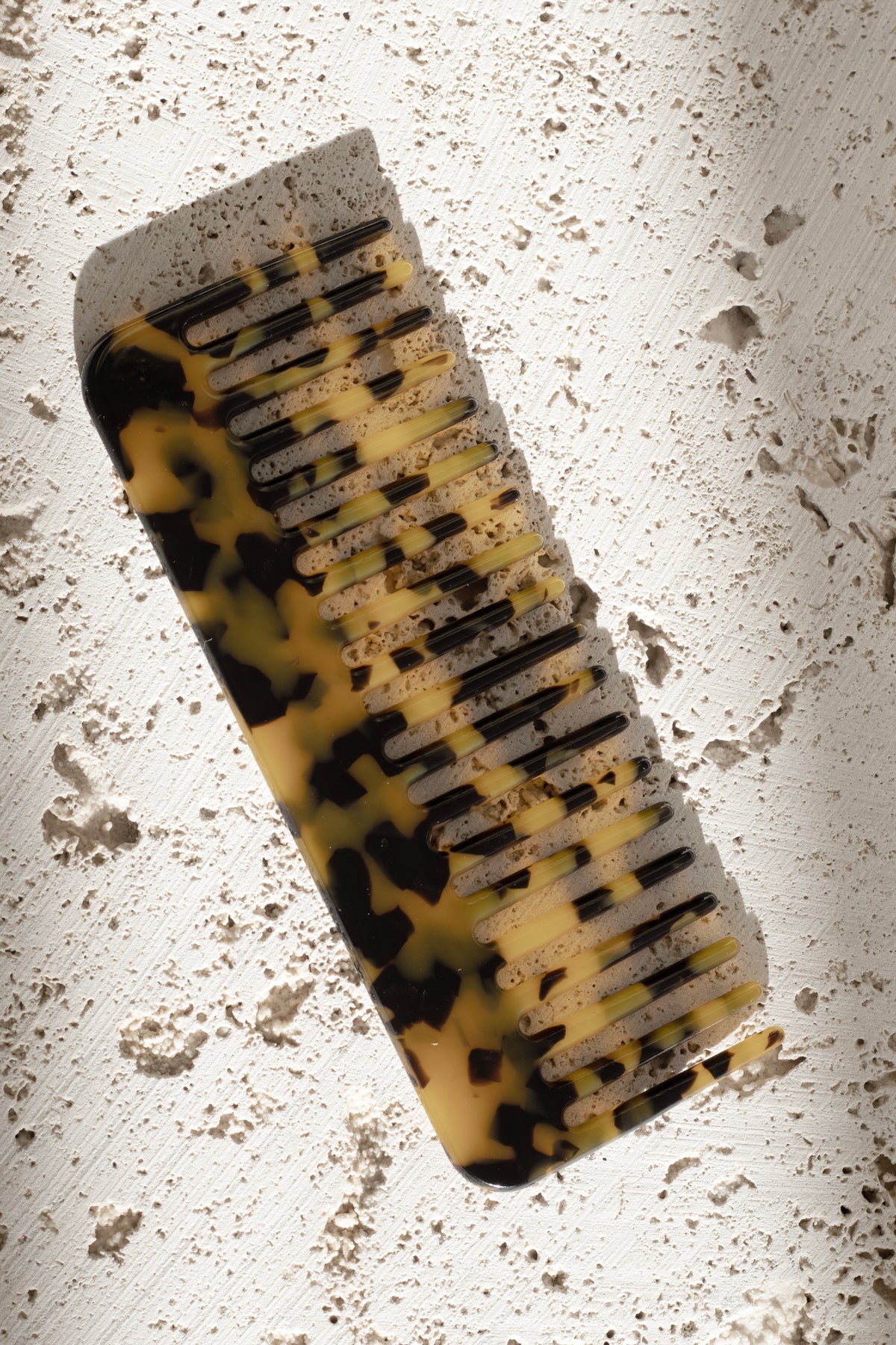 Light tortoiseshell acetate comb in amber and brown on a travertine surface