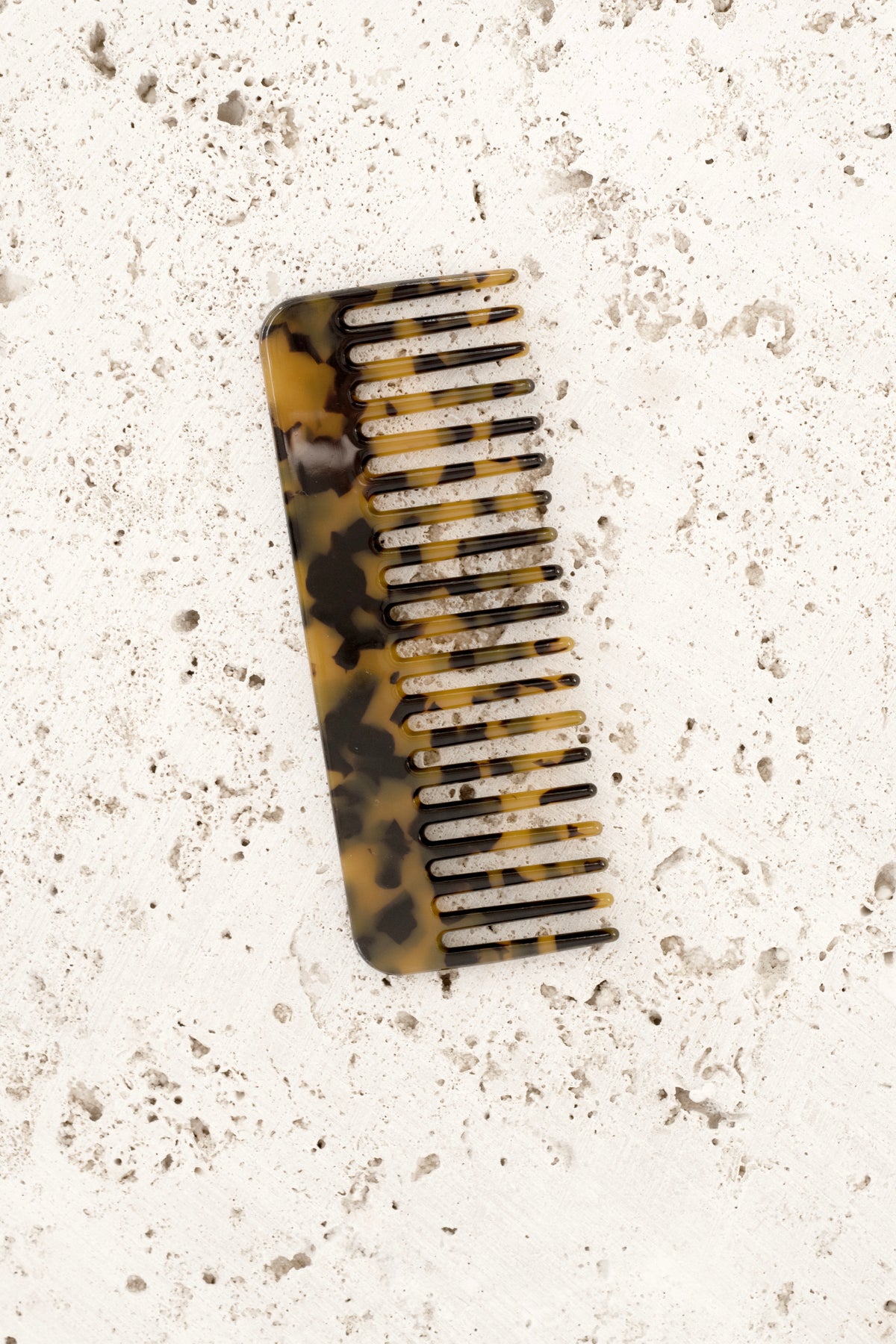 Dark tortoiseshell acetate comb on travertine, angled to show the spine