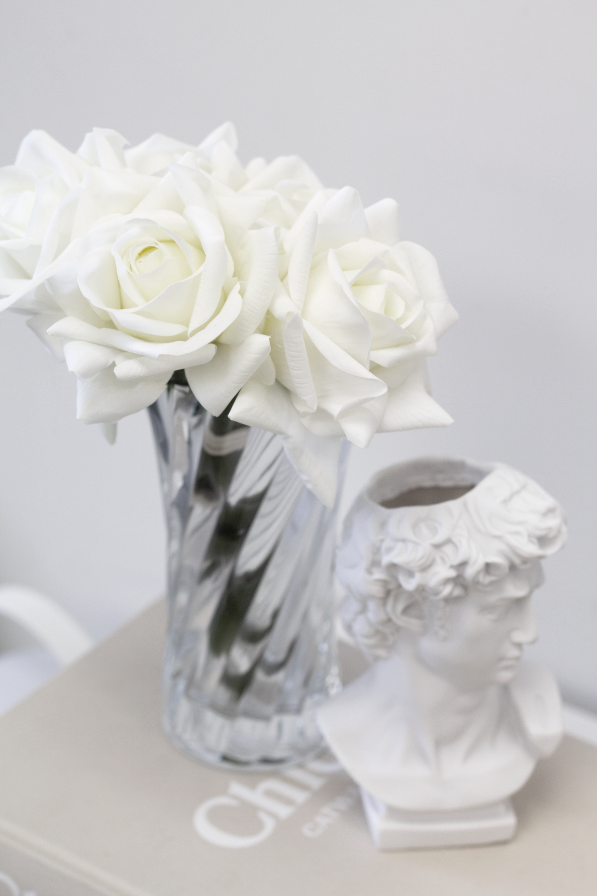 David bust vase beside a marbled vase of white roses on a side table