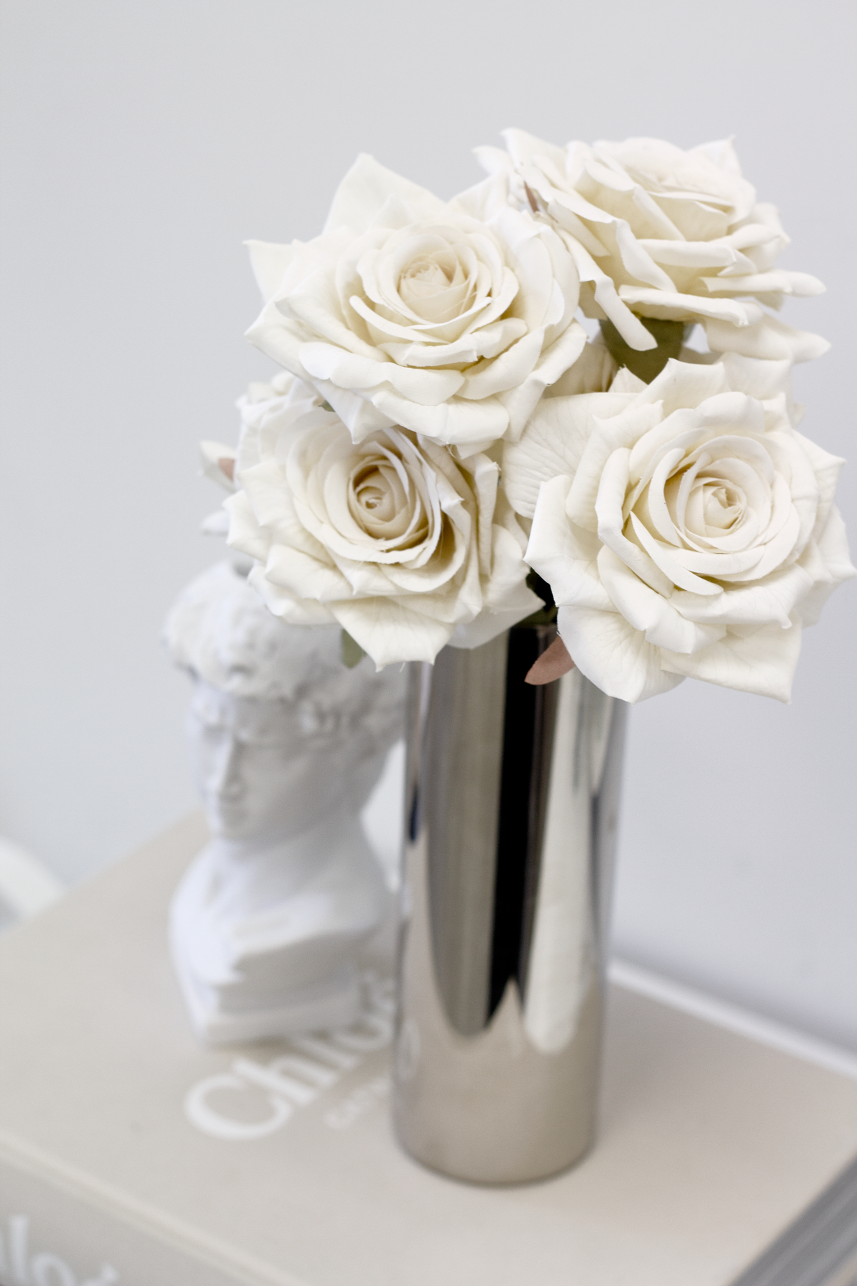 Champagne roses in a tall silver vase beside a white bust