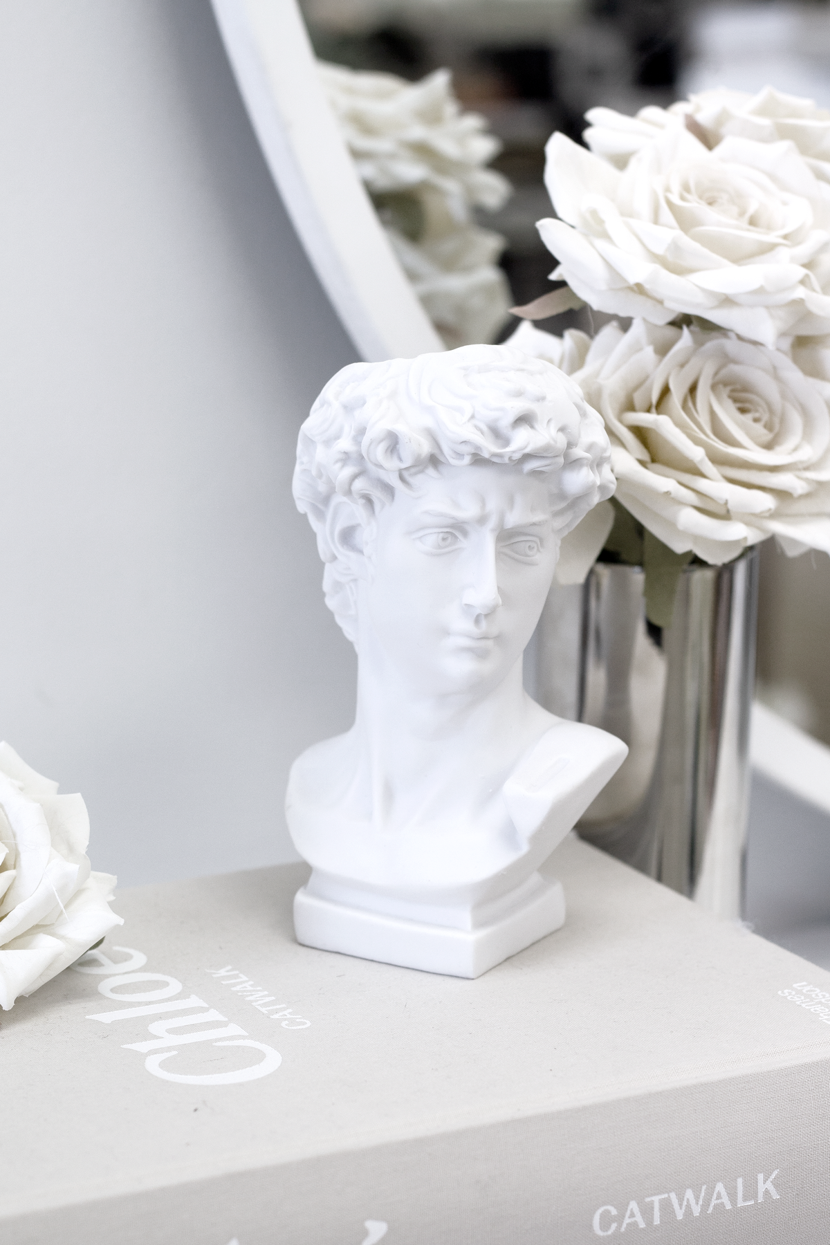 David bust vase in front of a round mirror with white roses reflected behind