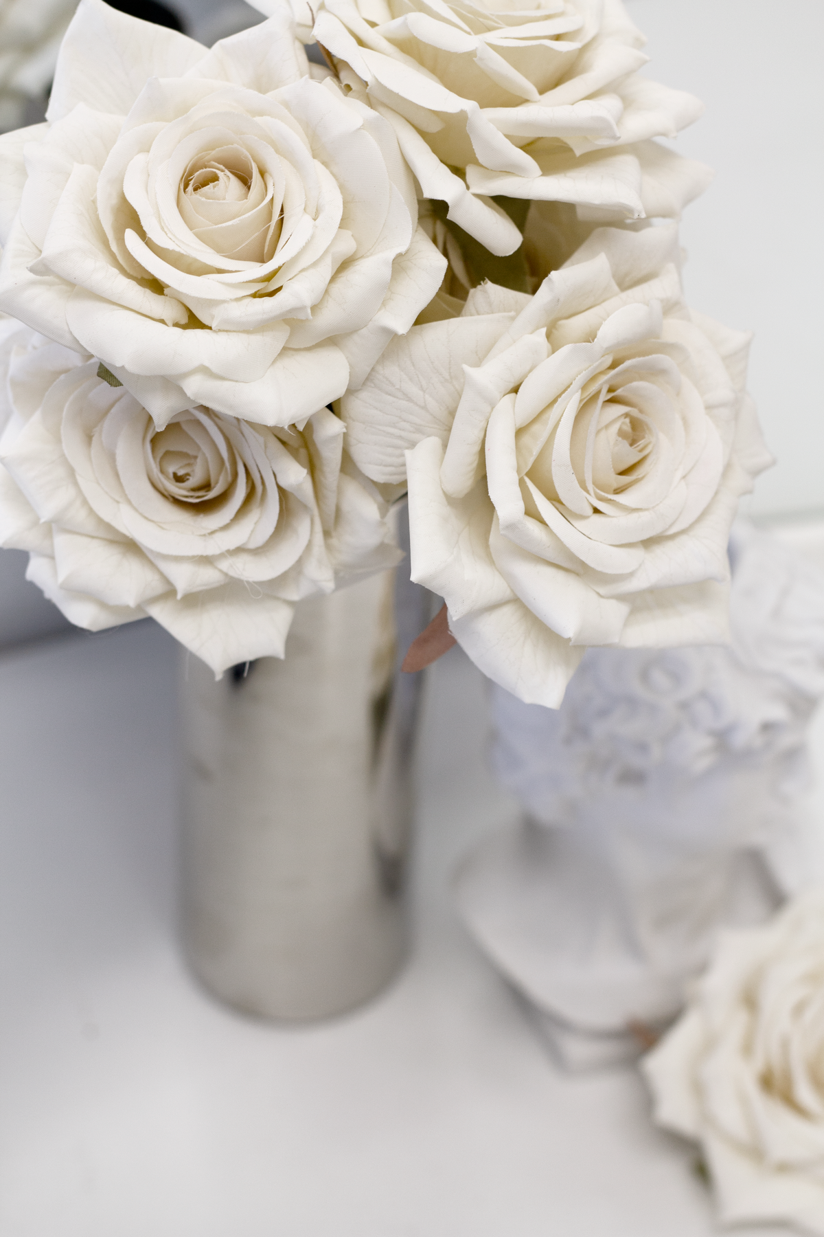 Champagne roses in a silver vase beside a white bust, close view