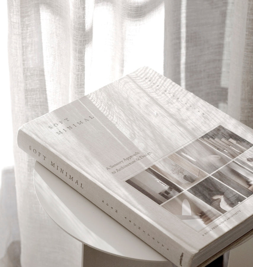 Soft Minimal lying closed on a pale round table by a window, dappled light across the cover