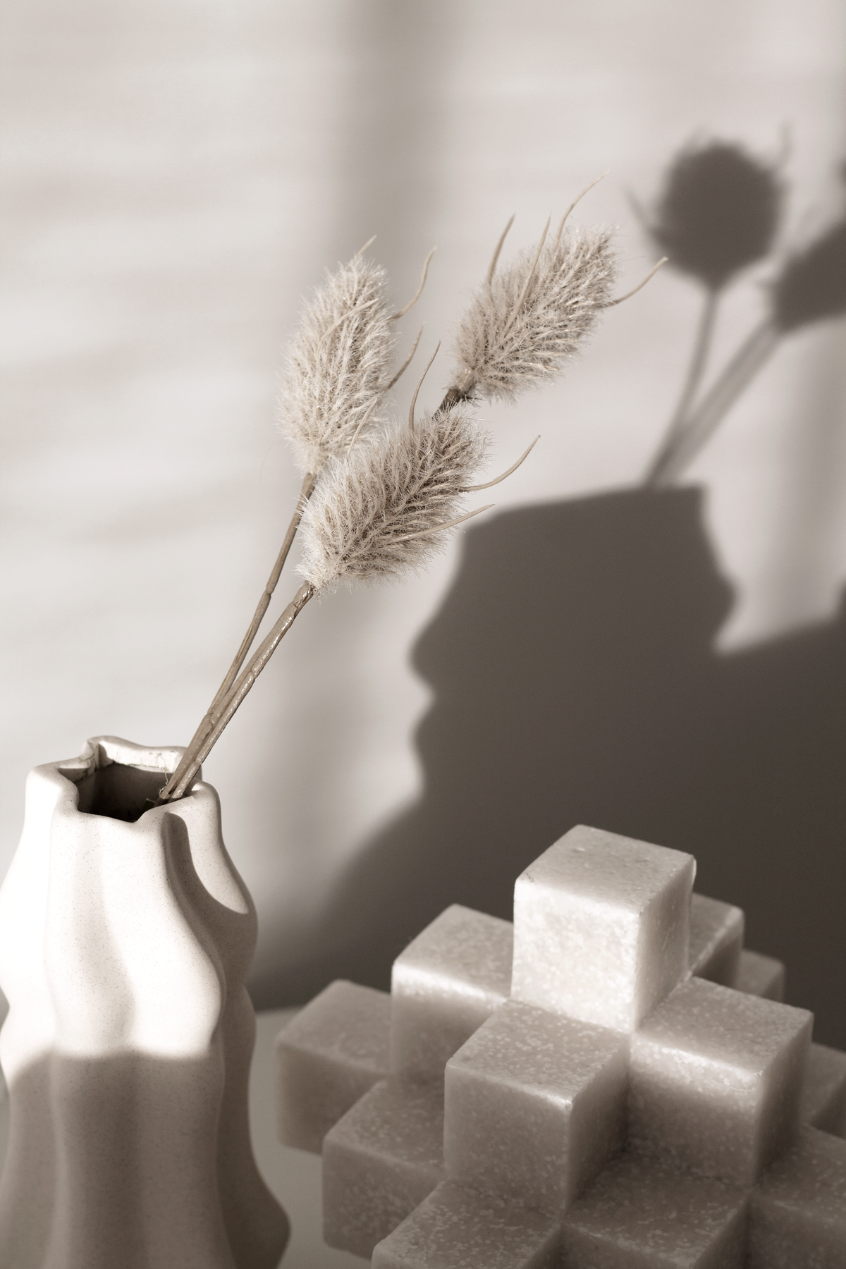 Faux bunny tails in a white vase casting shadows beside a marble cube sculpture
