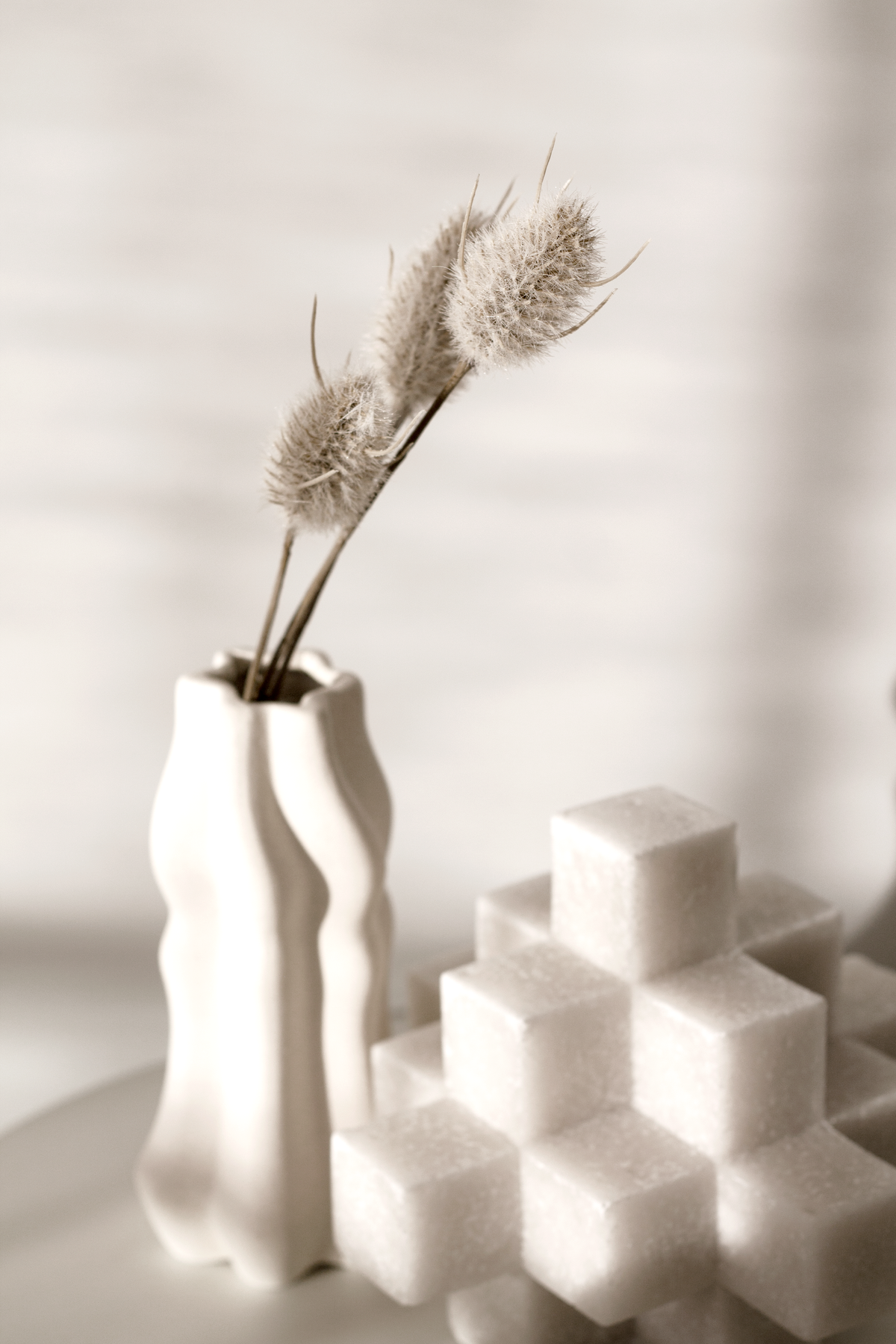 White Cubism sculpture beside a fluted vase of dried grasses on a tray