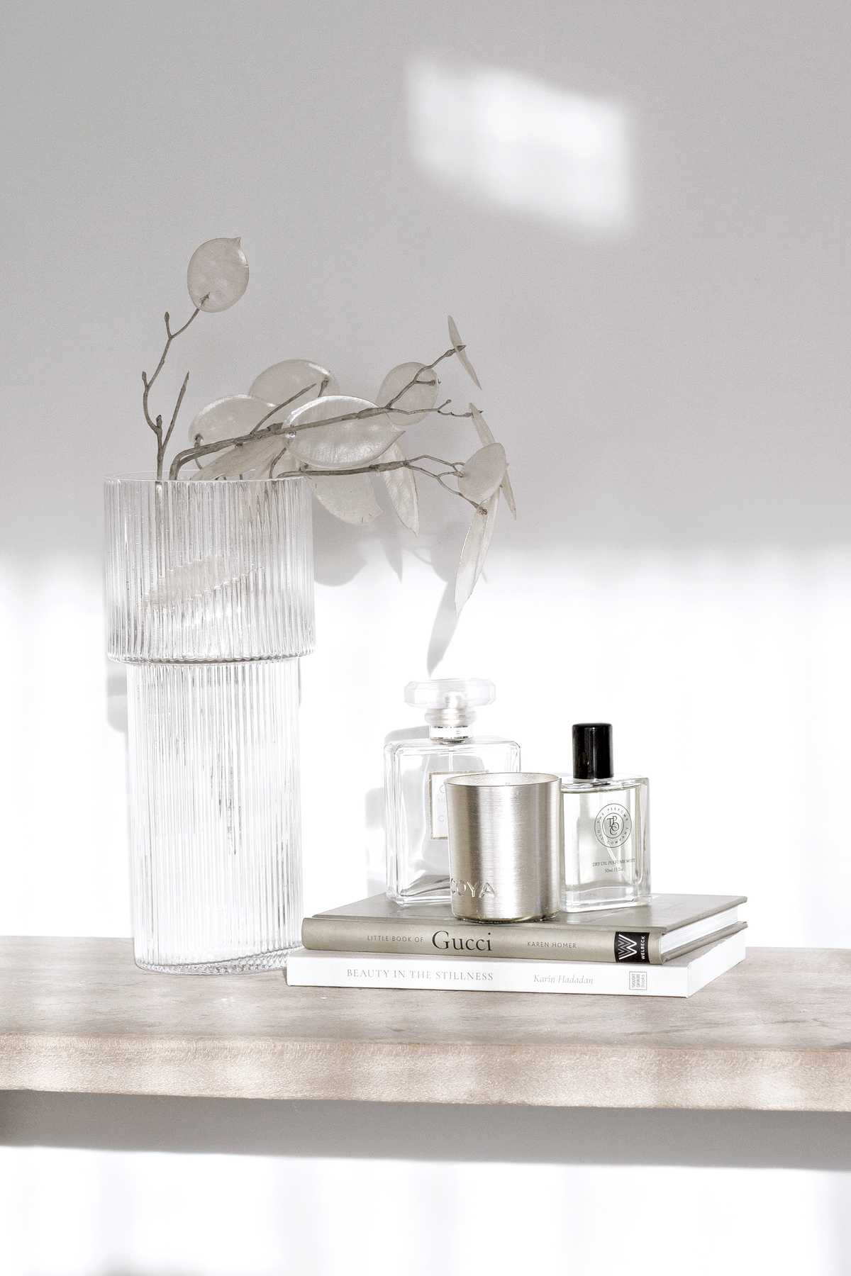 Tall ribbed glass vase of dried stems on a shelf beside perfume bottles on a book