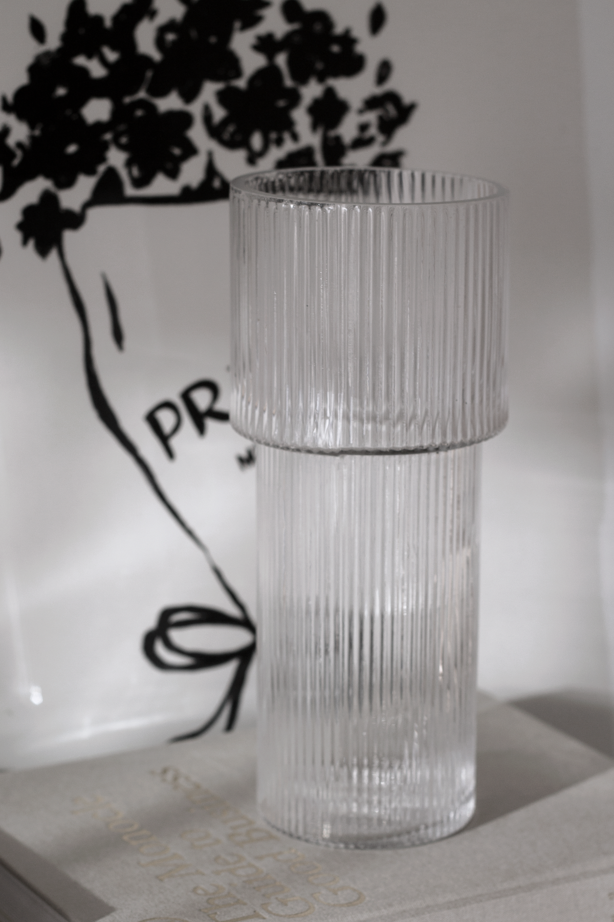 Ribbed glass vase in front of a framed line drawing with dark foliage above