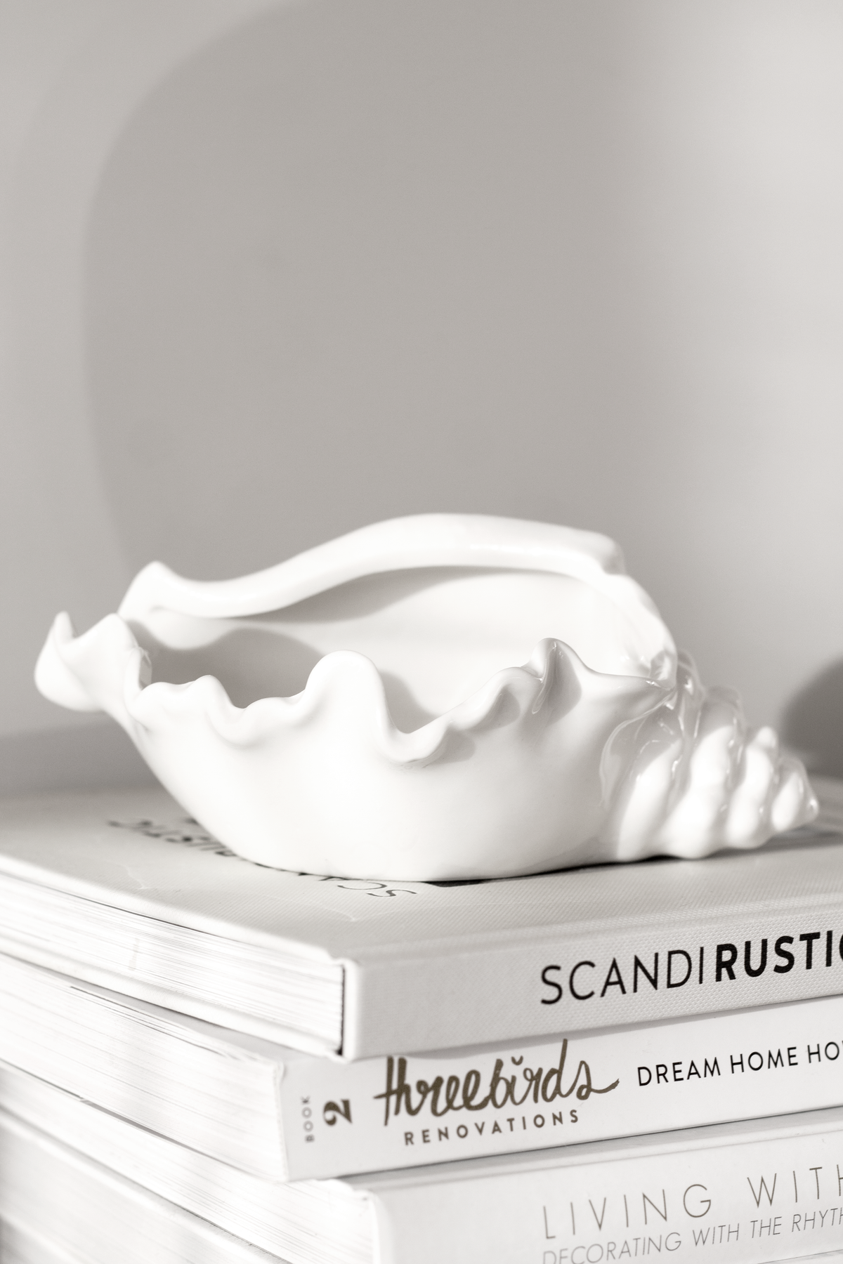 Conch bowl on a stack of interiors books against a plain pale wall