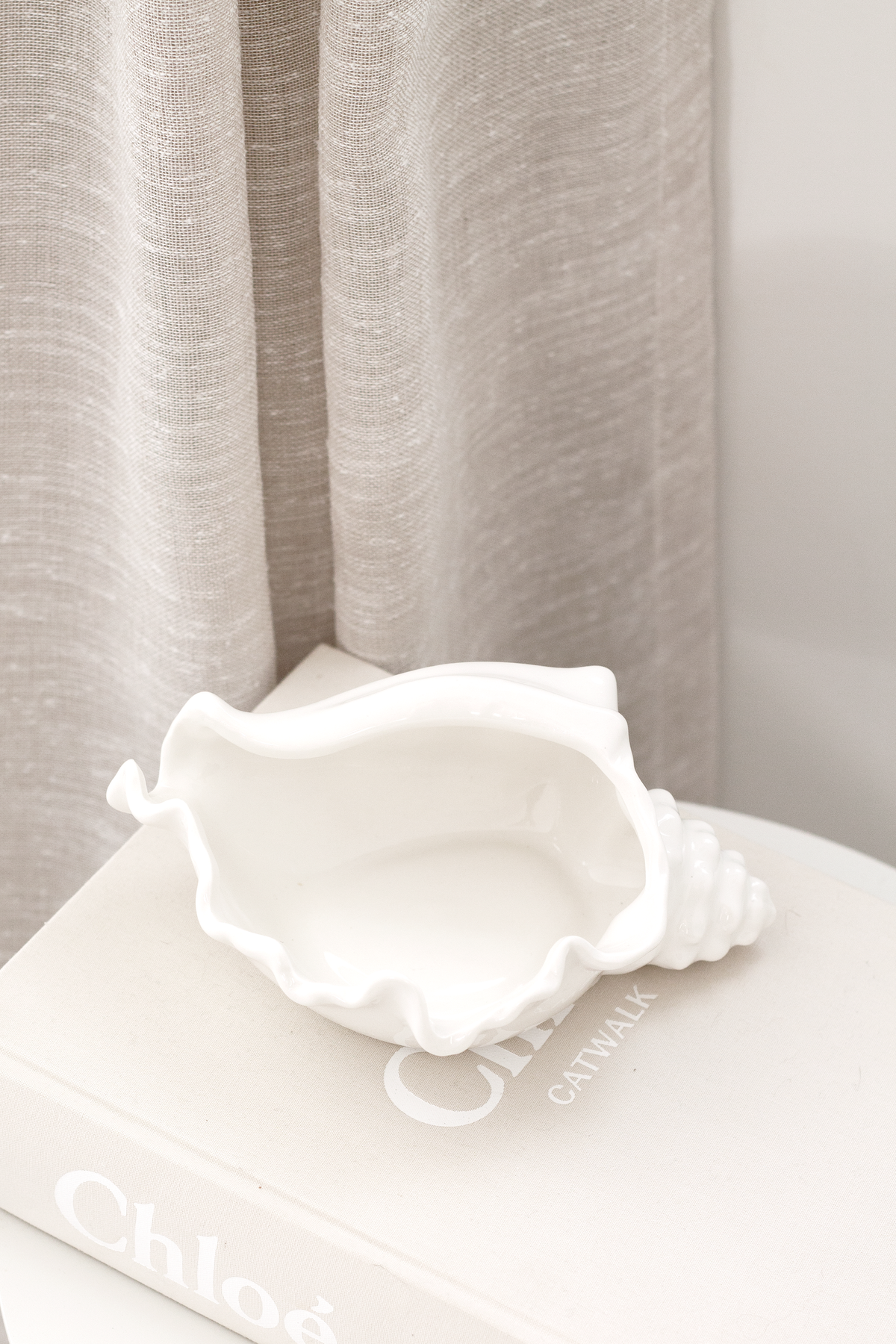 Conch bowl on a book with grey linen curtains falling behind