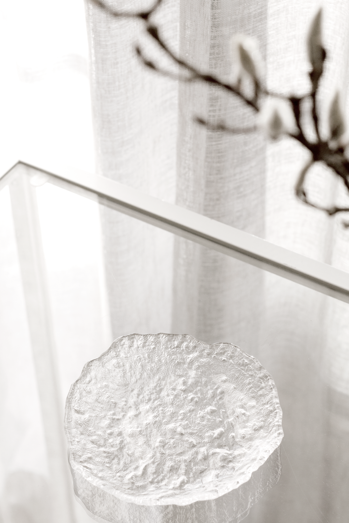 Glacier glass tray on a clear acrylic table by a sheer curtain with branches above