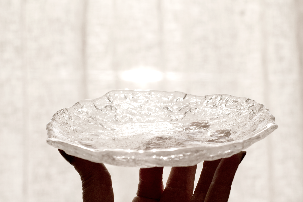 A hand holding the Glacier glass tray up to the light, showing its rippled edge