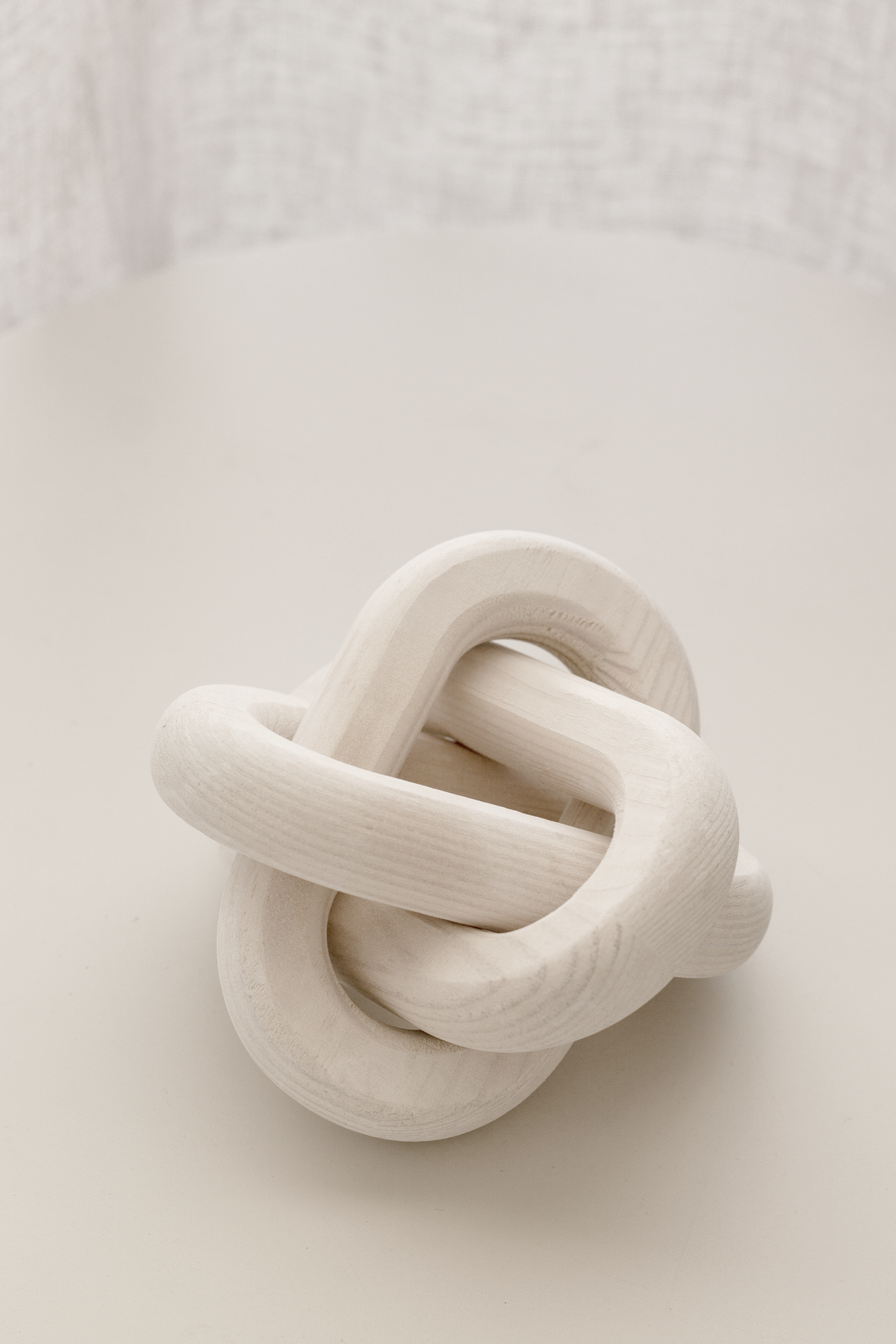 White knot ornament on a pale surface with linen hanging behind it
