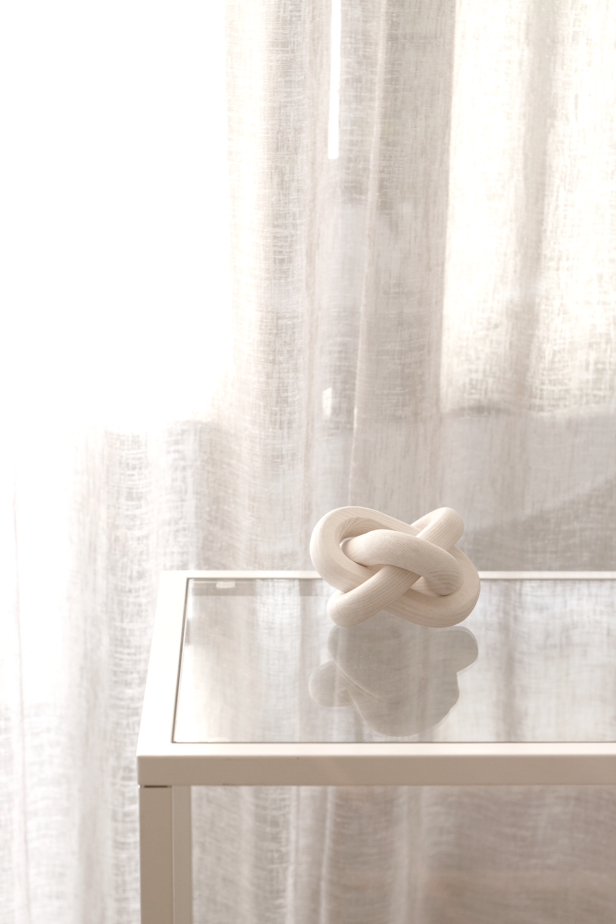 Knot ornament on a glass topped table beside a bright window and curtain
