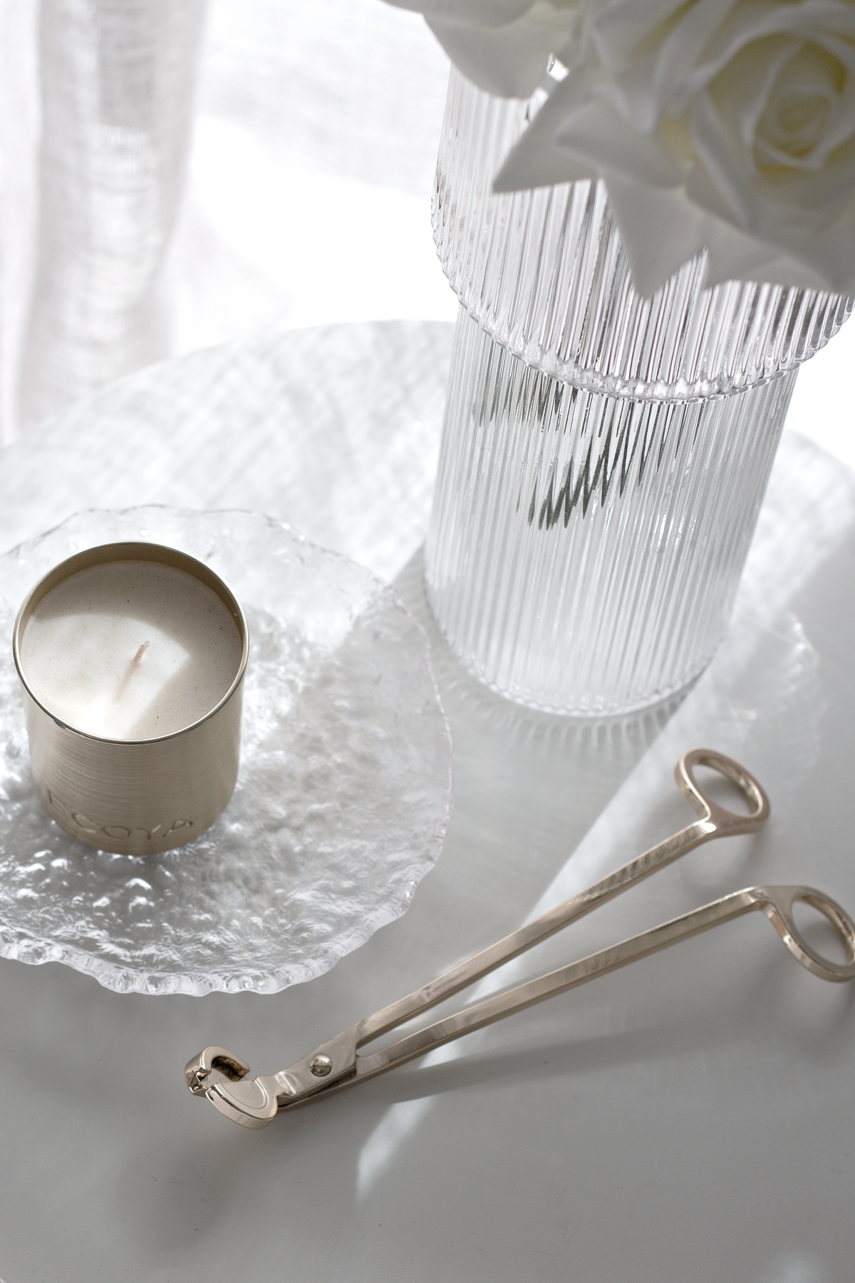 Glacier glass tray with a candle, a ribbed glass and gold tongs on a white surface