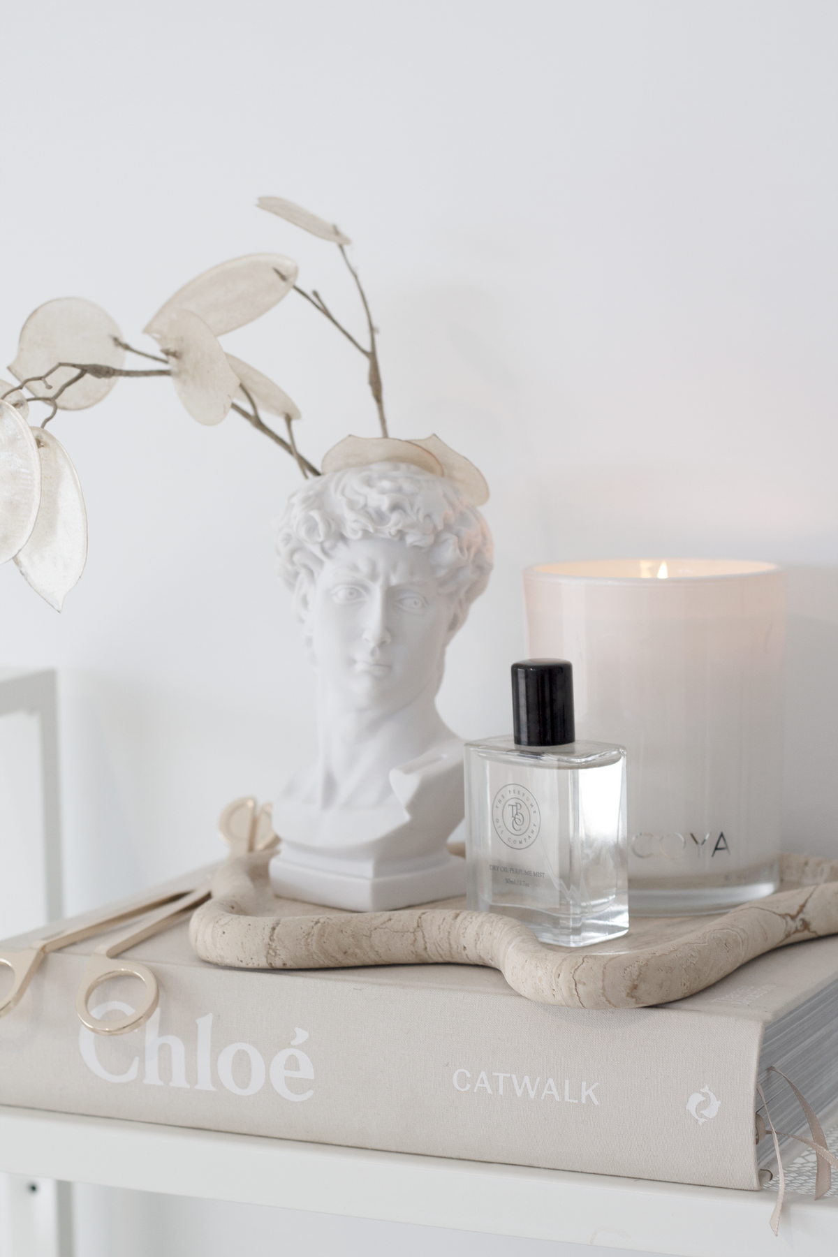 David bust vase holding dried stems beside a candle and a perfume bottle on books