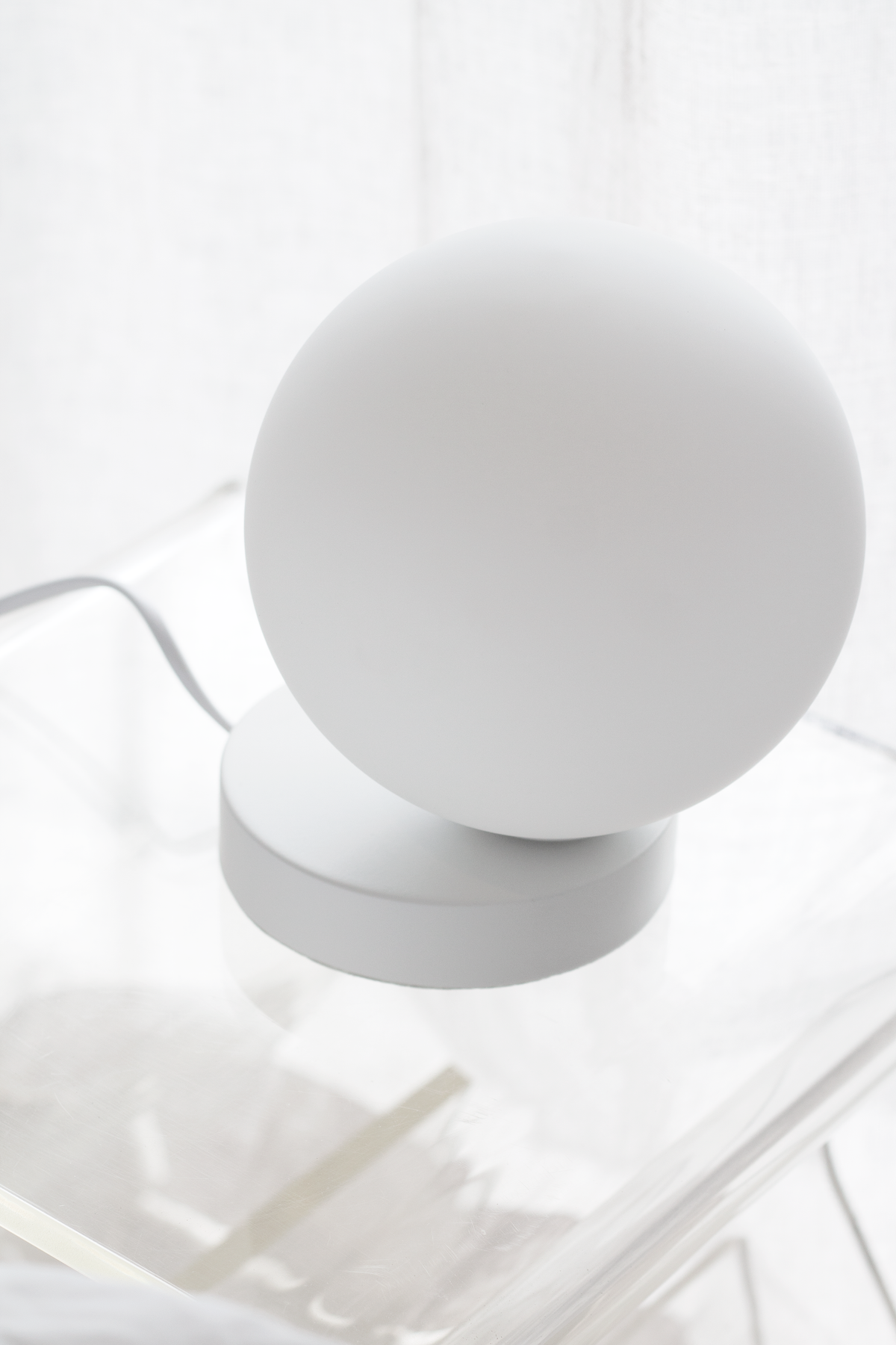 Yuri Table Lamp with its frosted glass globe on a clear surface in bright light