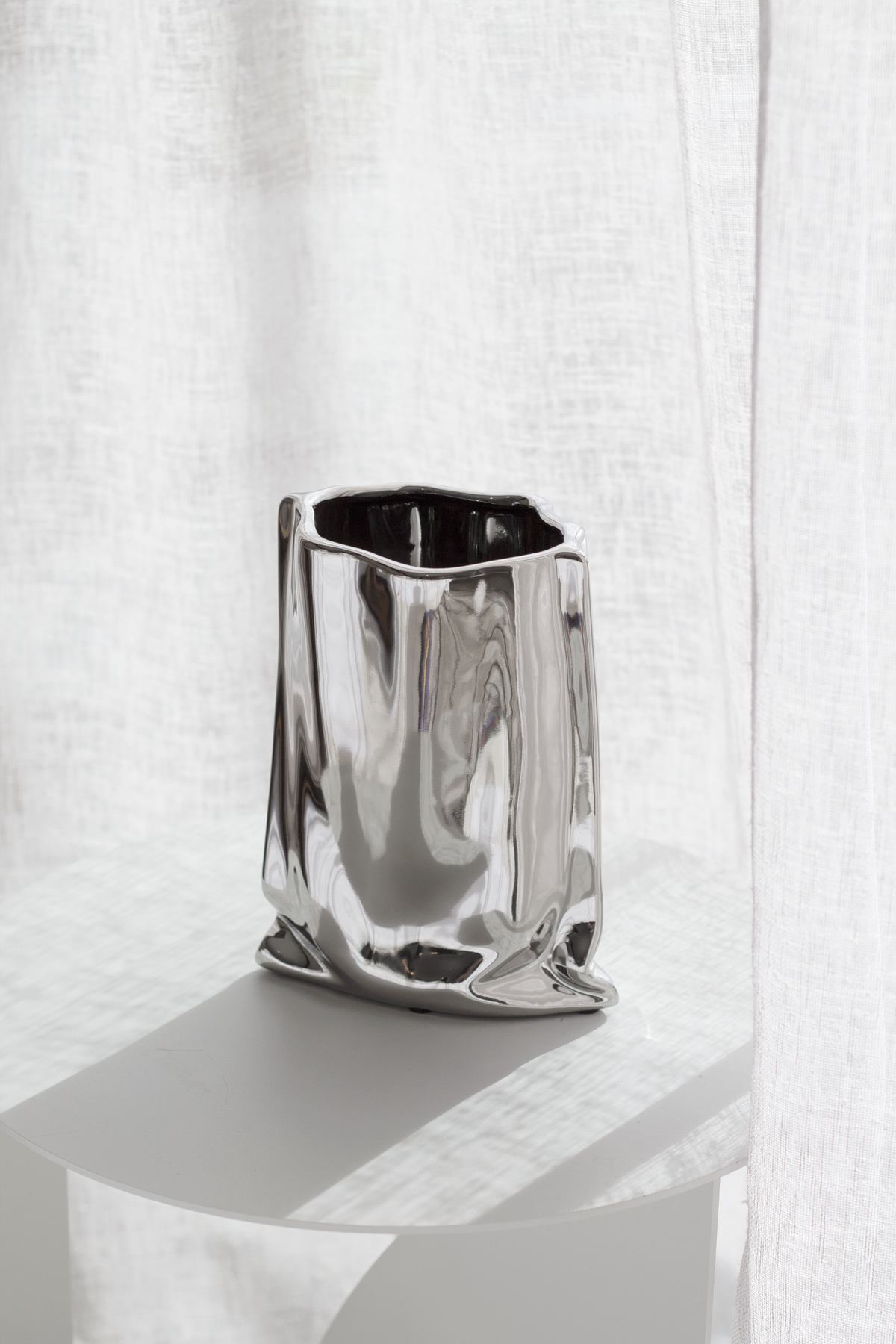 Silver metallic bag vase on a white plinth against a linen backdrop