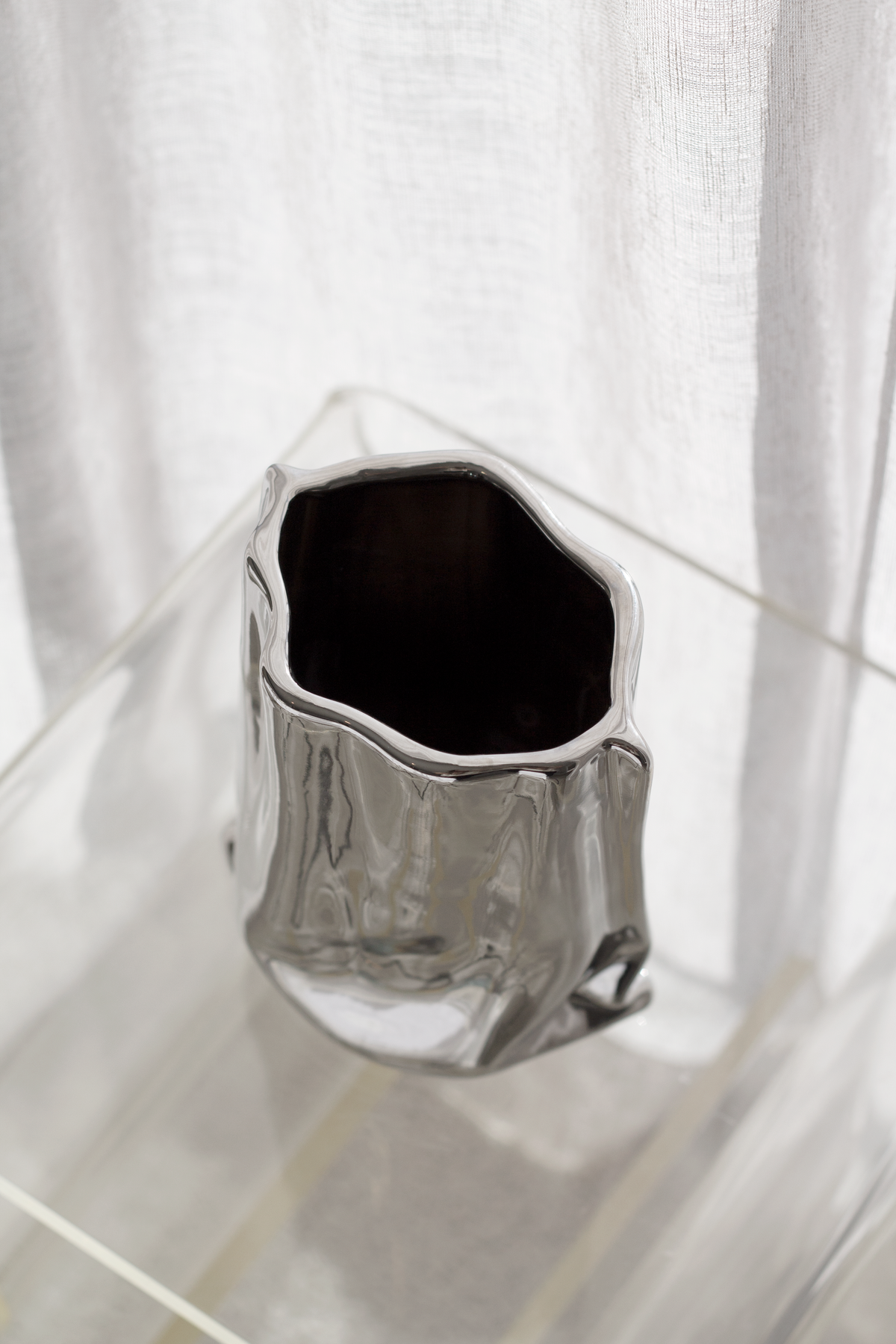 Silver metallic bag vase at a high angle on a clear table, dark interior showing