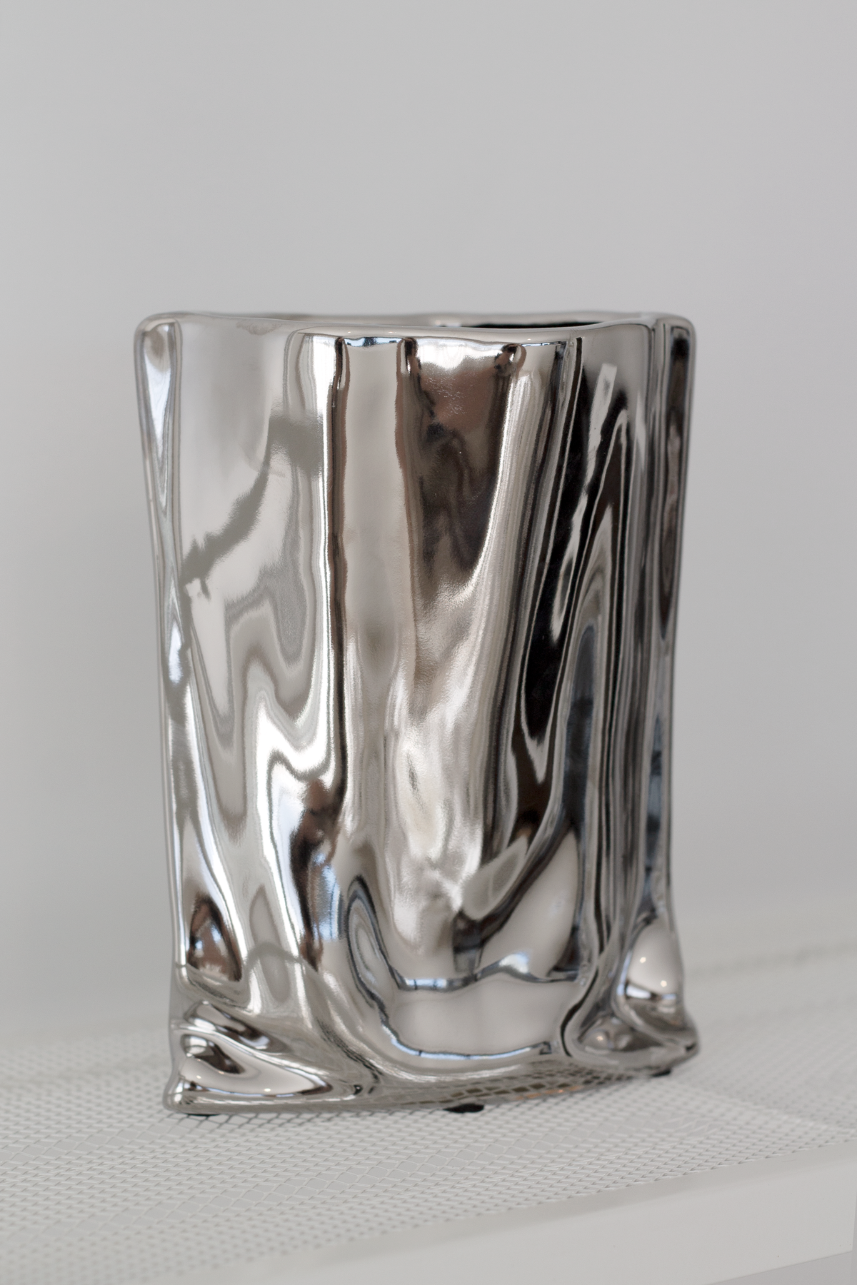 Silver metallic bag vase on a white ledge, sharp front view of the mirrored folds