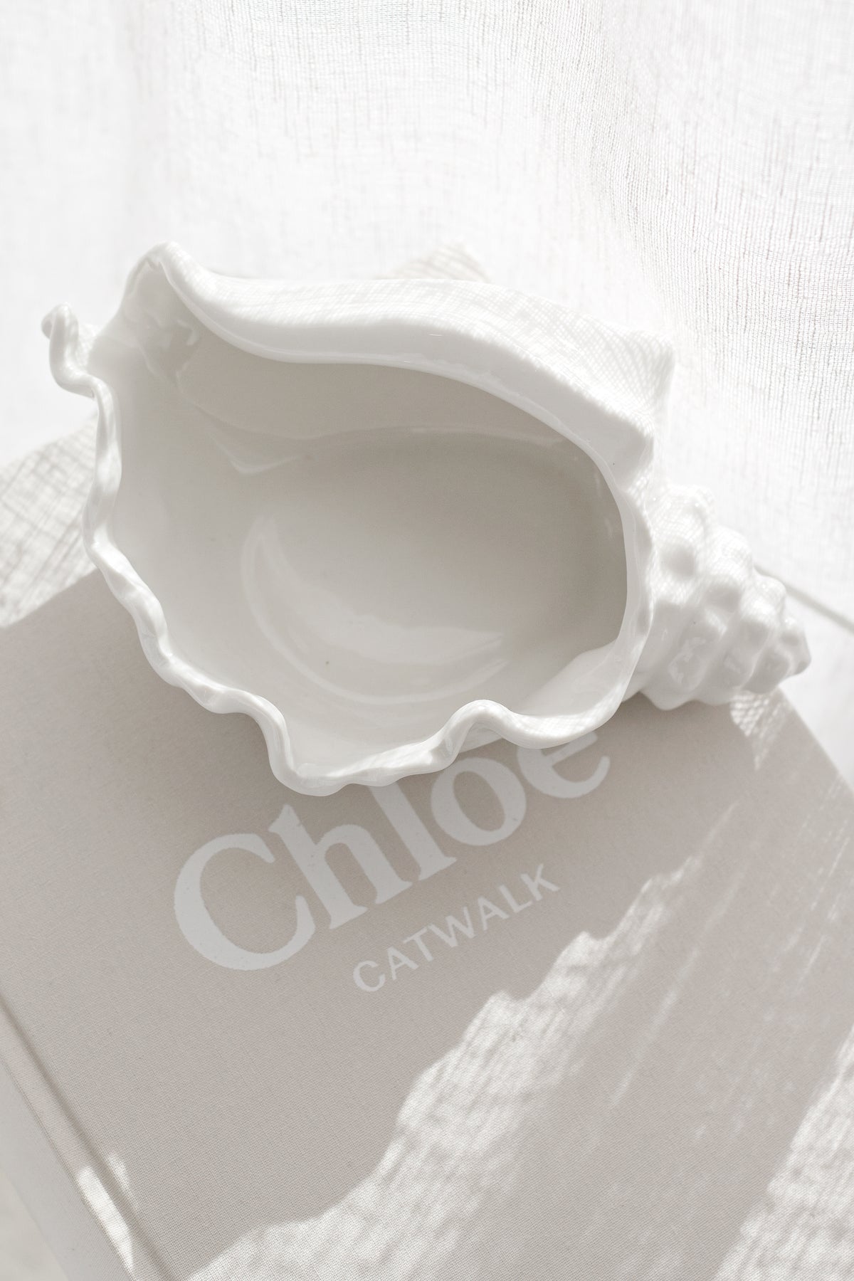 Looking down on the conch bowl as it sits on a fashion book against pale linen