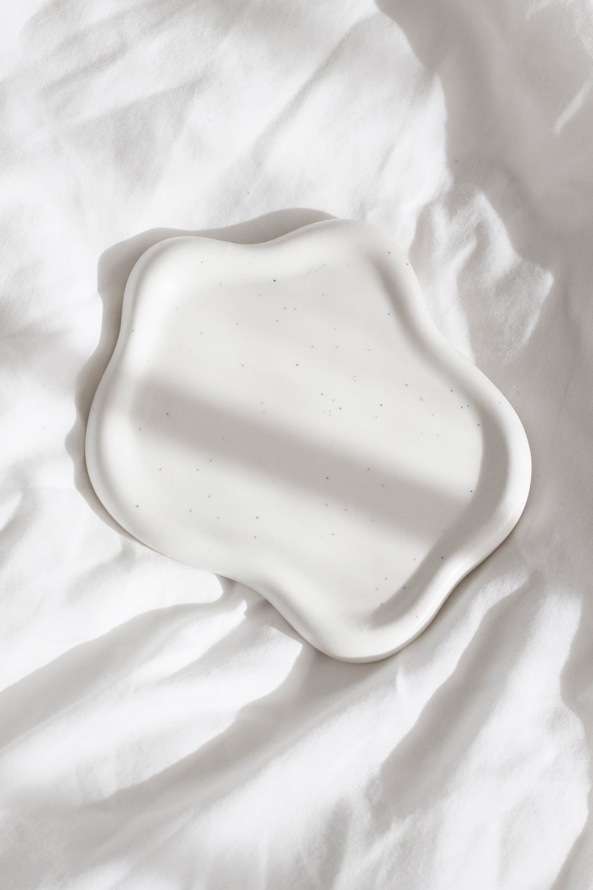Empty white cloud trinket dish on crumpled white bedding