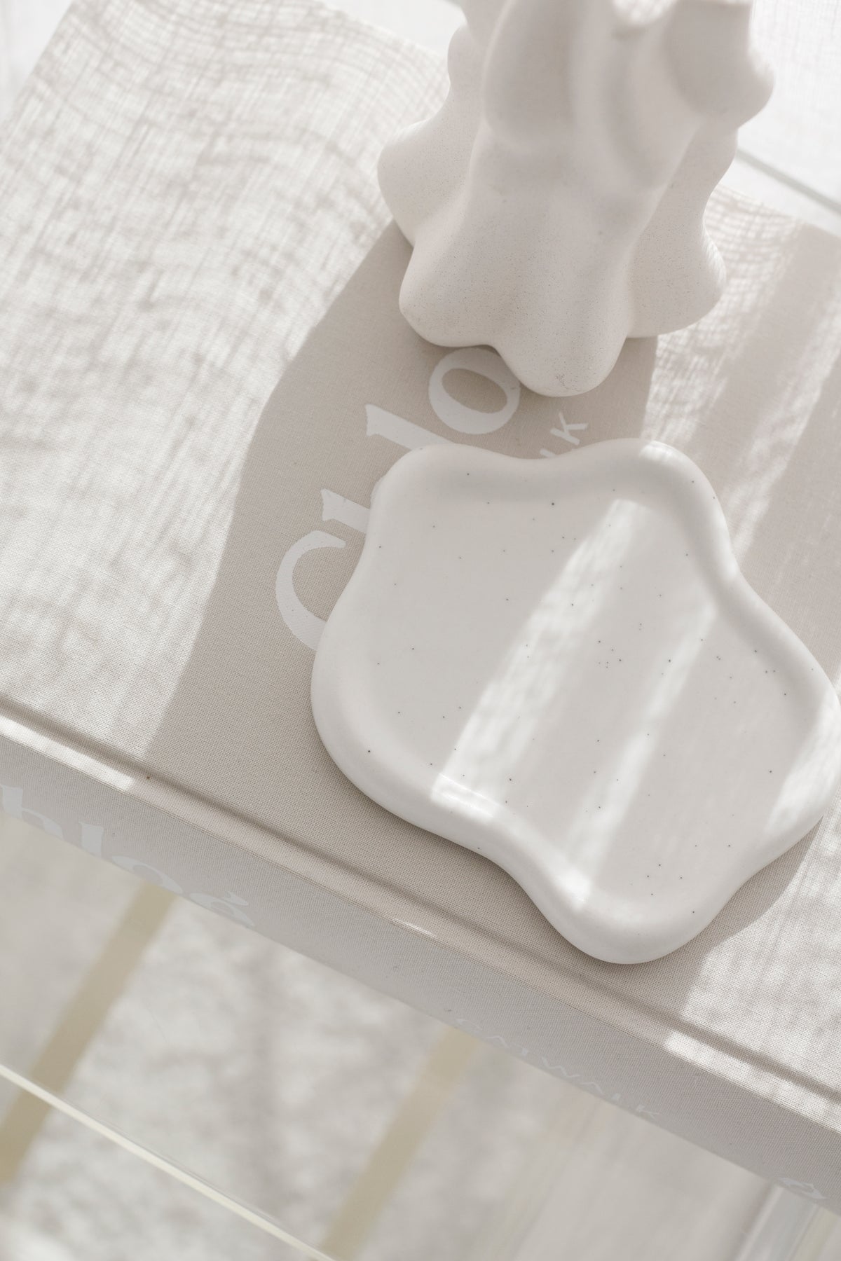 White cloud trinket dish on a glass shelf beneath a fluted vase