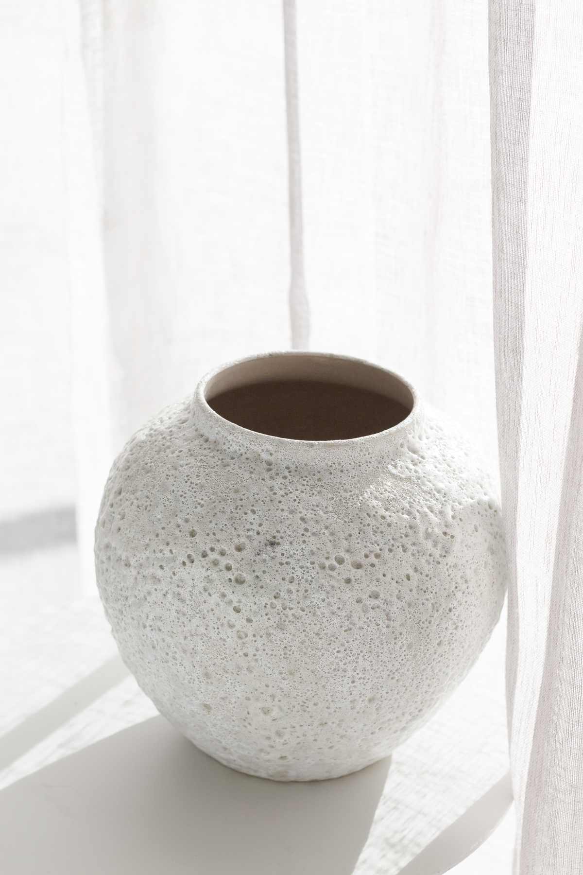 Short Seafoam vase empty on a white ledge with a sheer curtain behind, dark interior visible