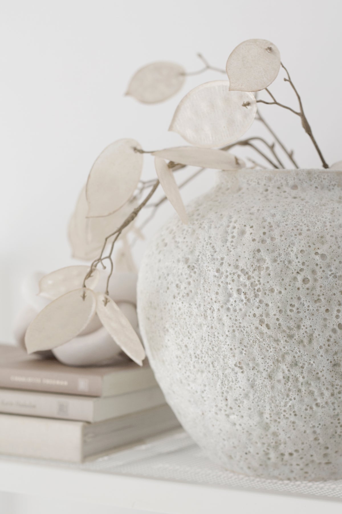 Close view of the short Seafoam vase with honesty stems resting on stacked books
