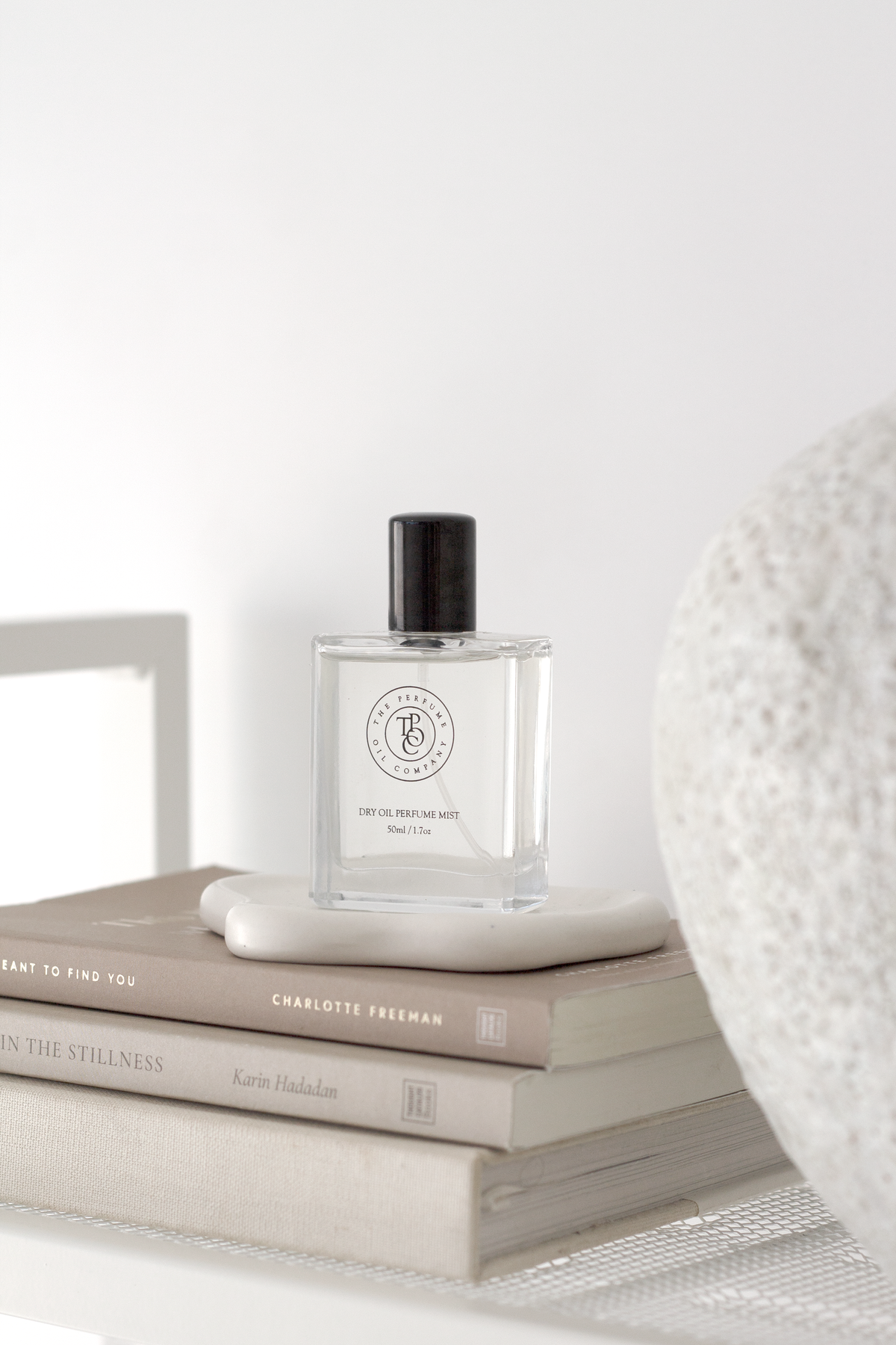 White cloud trinket dish with a perfume bottle on books beside a boucle cushion
