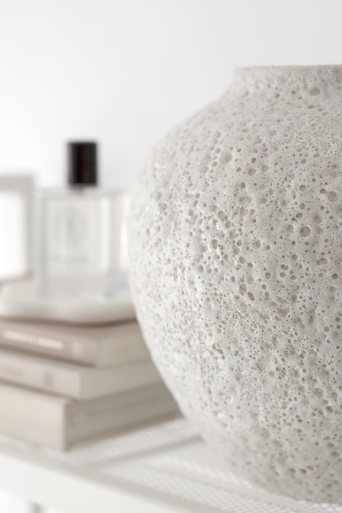 Close view of the Seafoam vase texture with a fragrance bottle on books behind