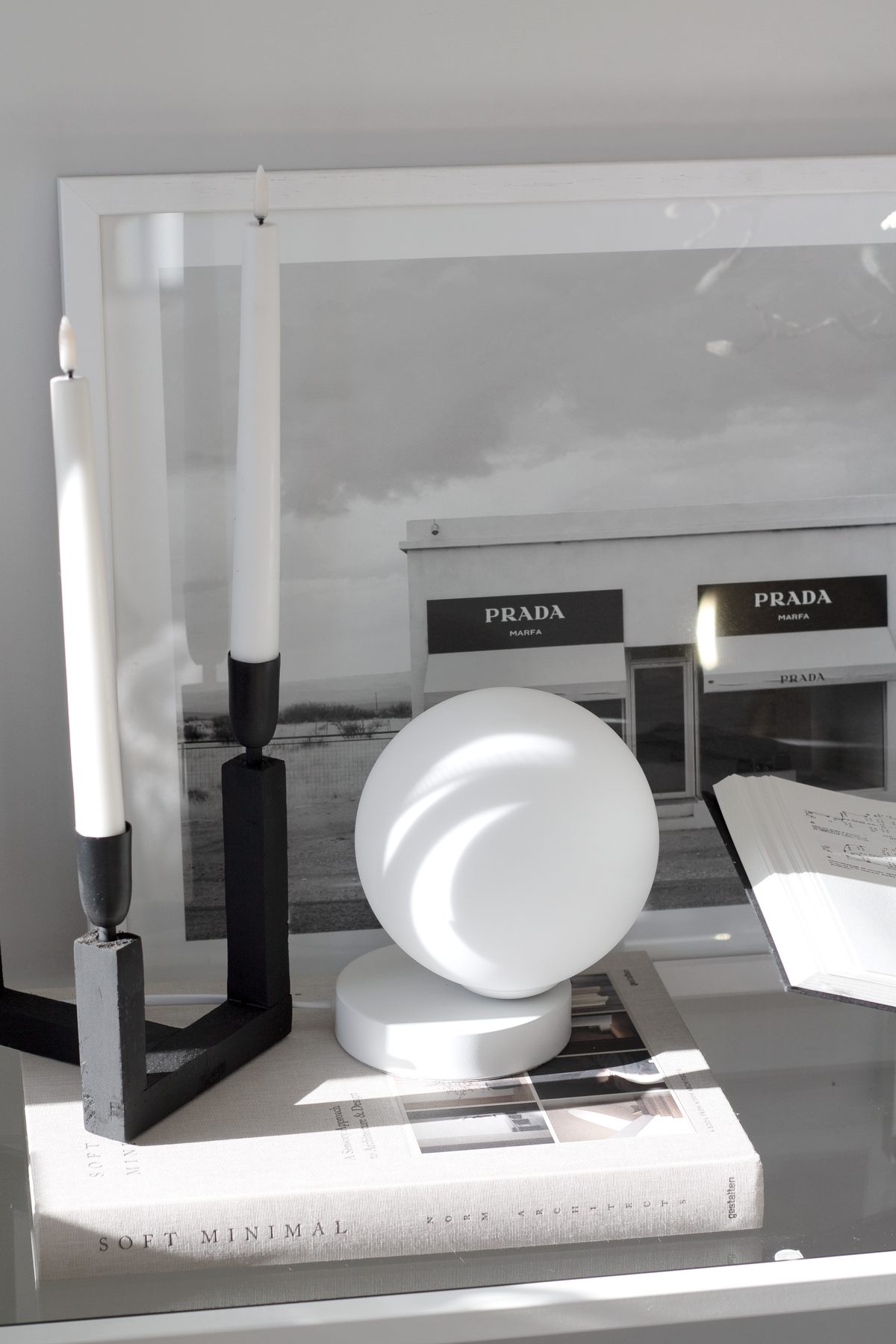 Black taper holders with white candles beside a round white lamp and a framed coastal photograph