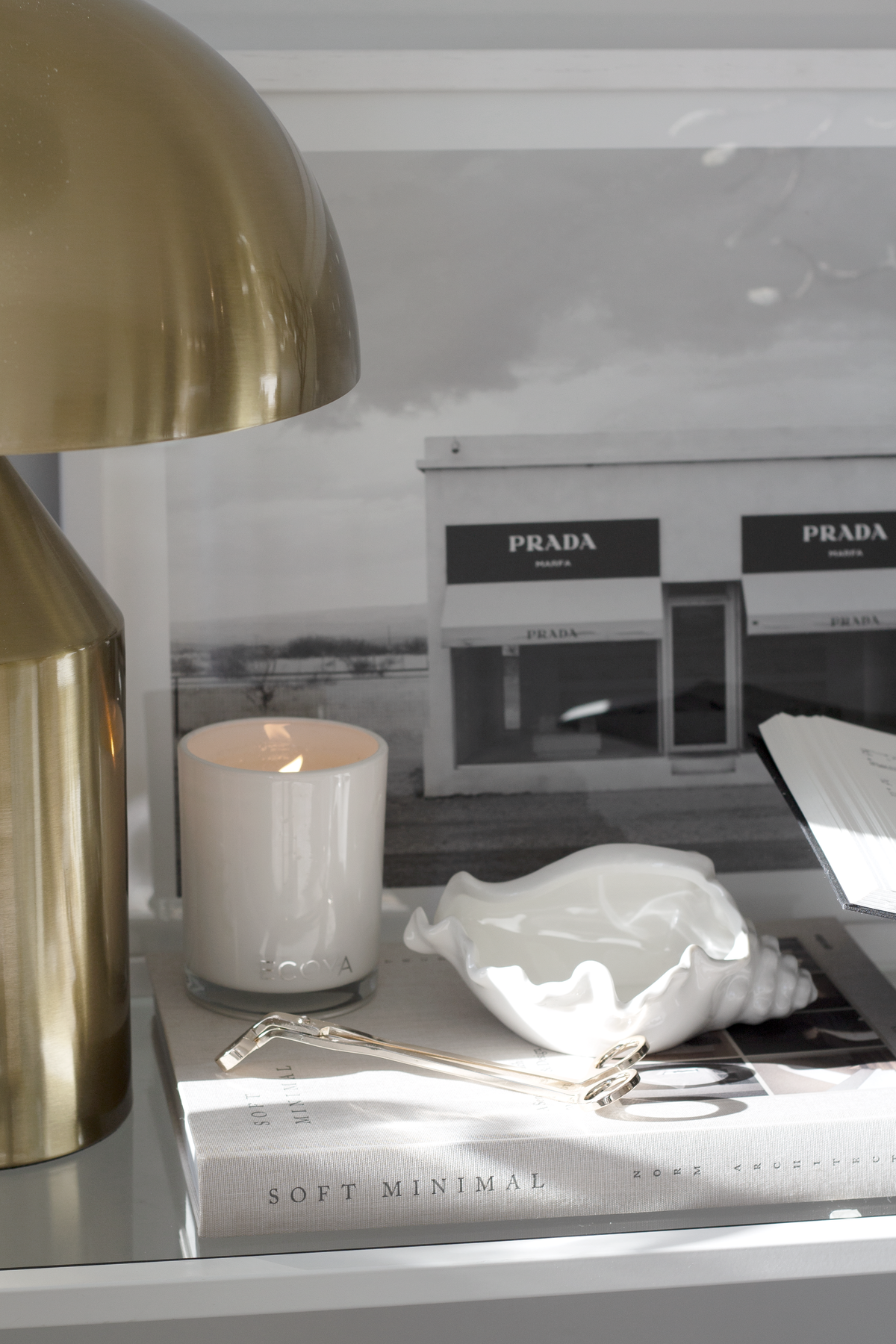 Conch bowl on a book beside a brass dome lamp, lit candle and framed print