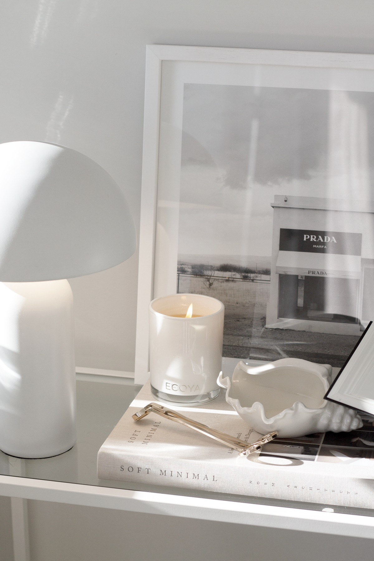 Conch bowl on a book beside a white dome lamp, lit candle and framed photograph on a shelf