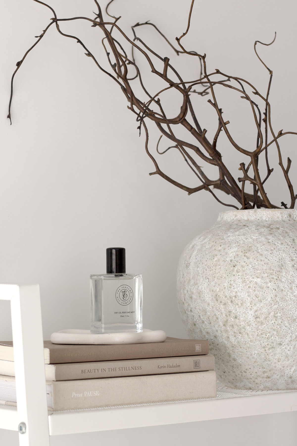 Wider view of the short Seafoam vase and branches on a shelf with books and a fragrance bottle