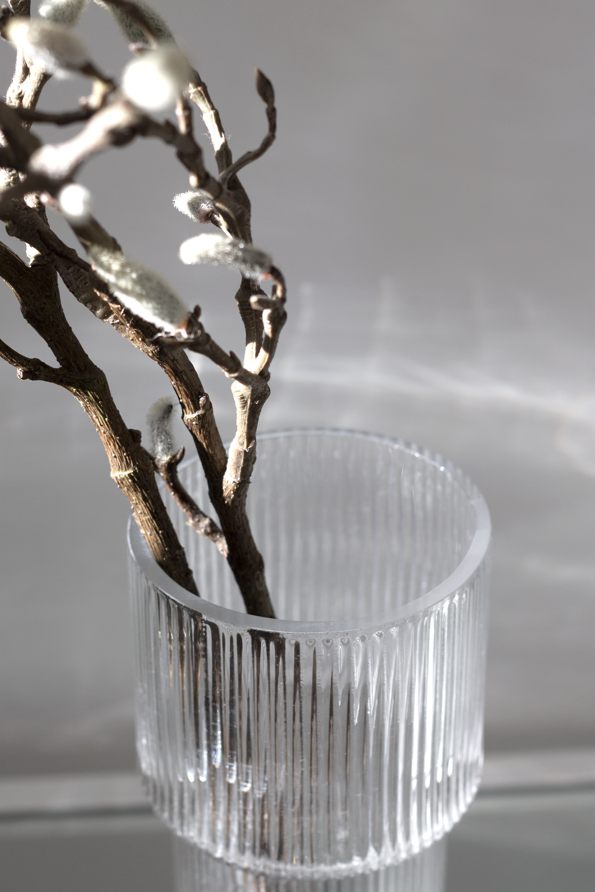 Close view of dark branches spilling from the ribbed glass vase