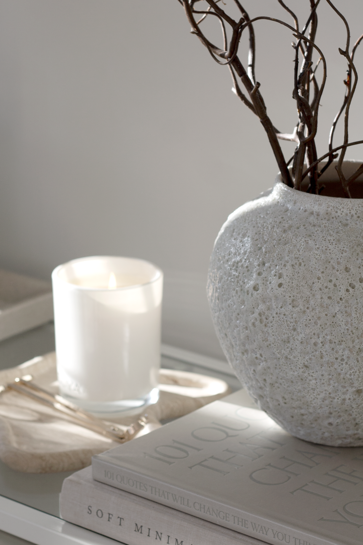 Short Seafoam vase of bare branches on books beside a candle on a wavy stone tray