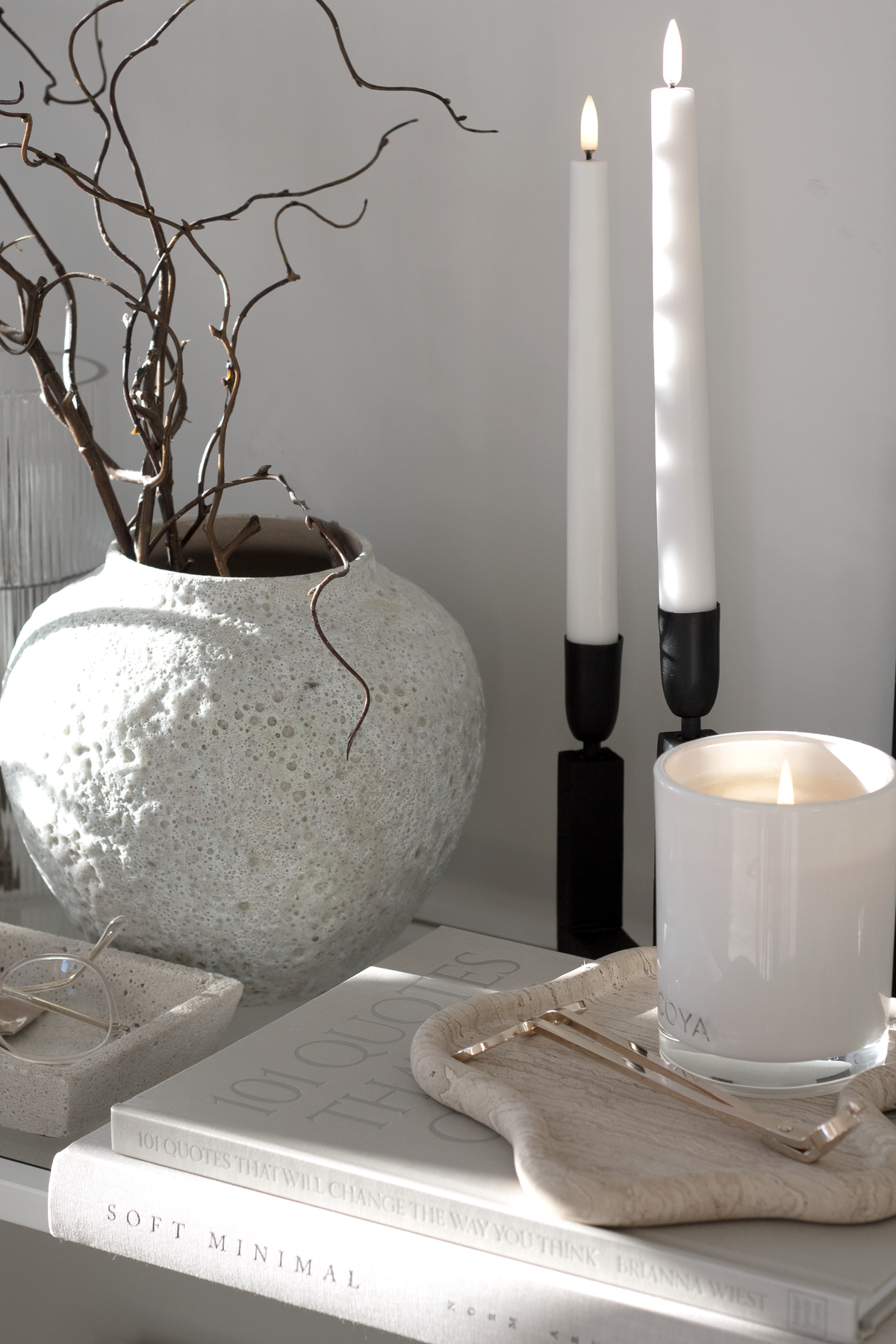 Short Seafoam vase of branches on books beside black candlesticks and a lit candle
