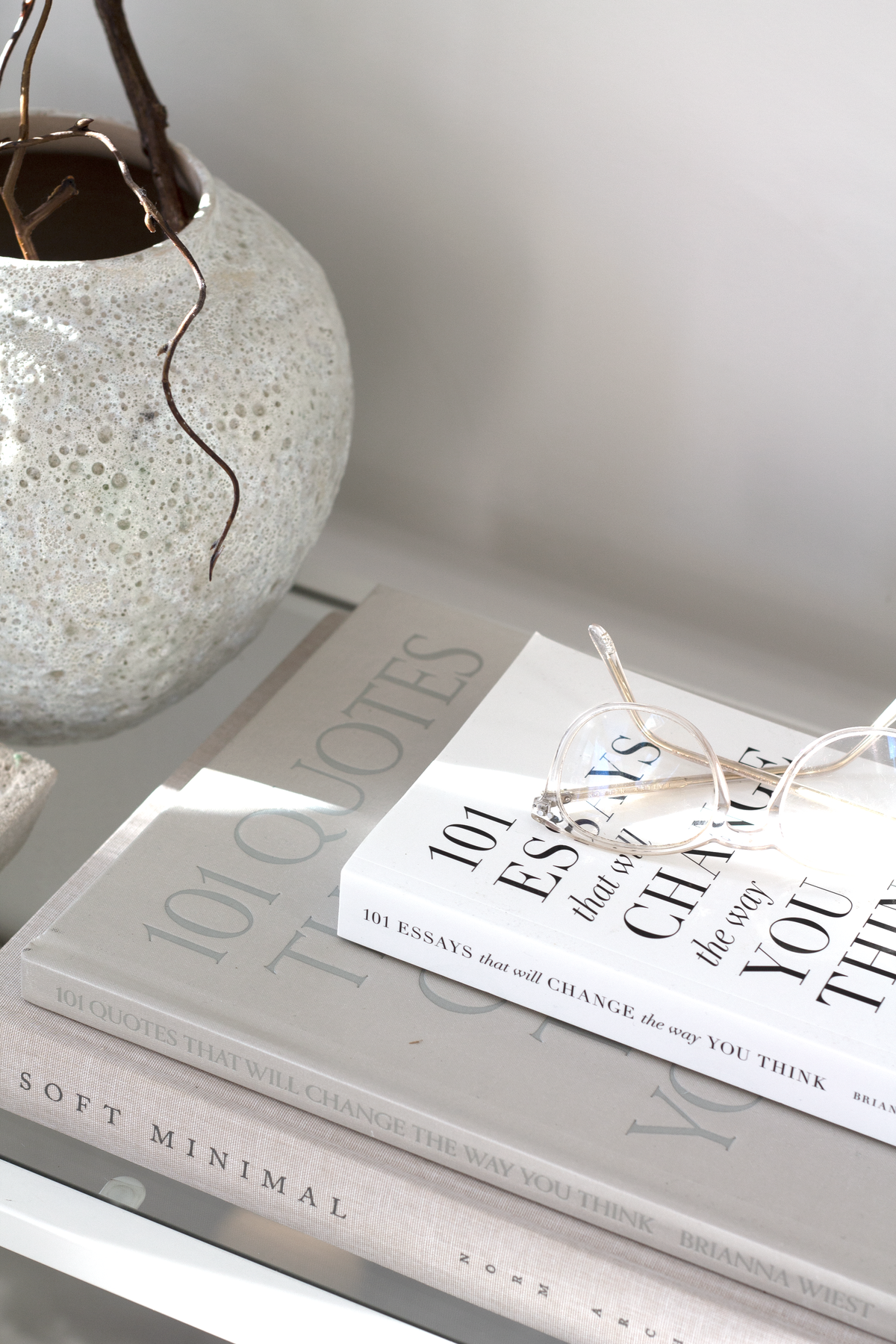 Short Seafoam vase of curly branches on a shelf above a stack of coffee table books