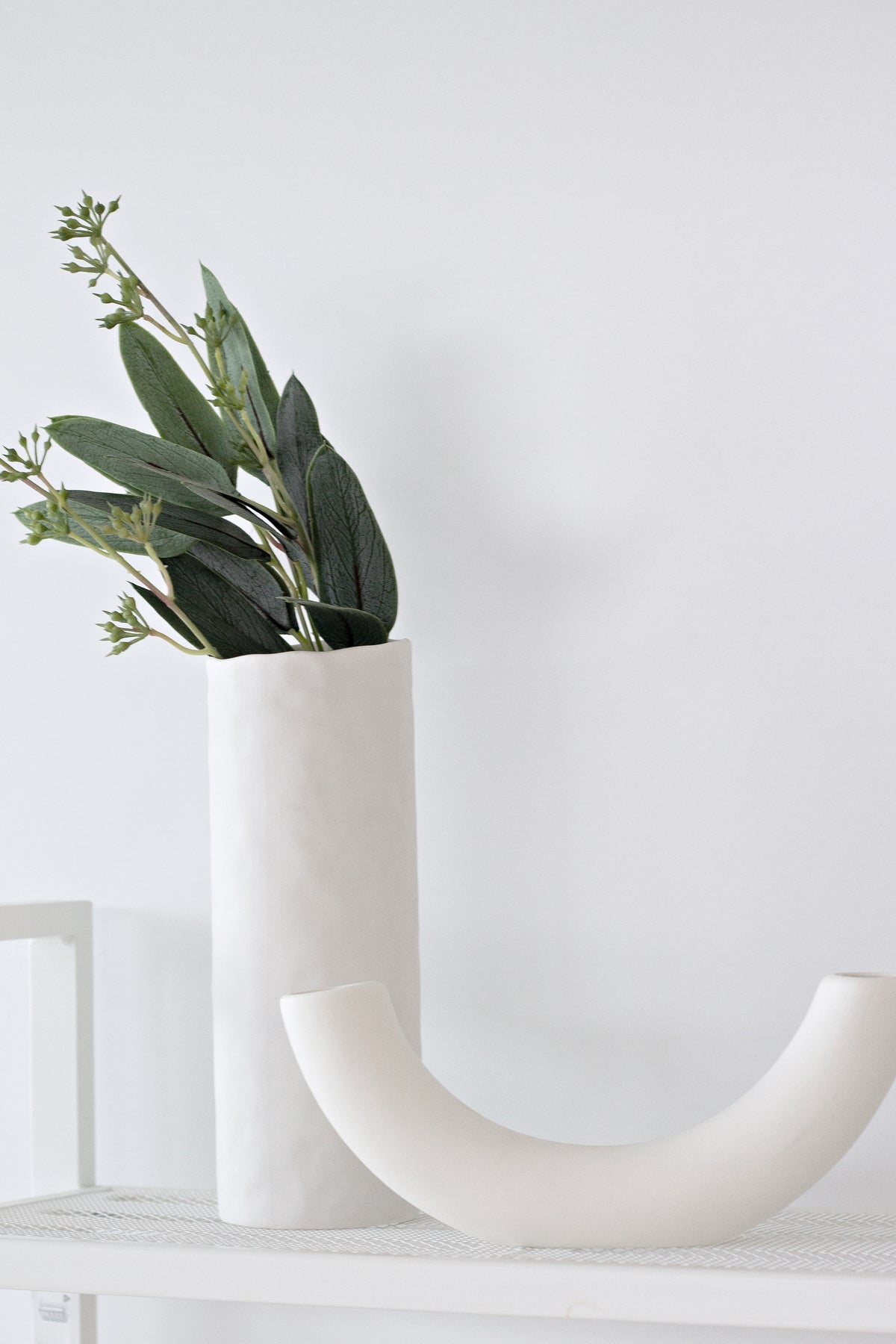 Half pipe vase in front of a textured cylinder vase holding eucalyptus stems