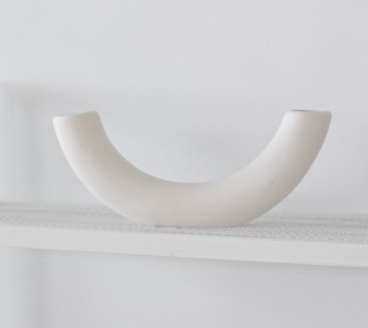 Half pipe vase side on atop a white shelf, the matte finish plain against the wall