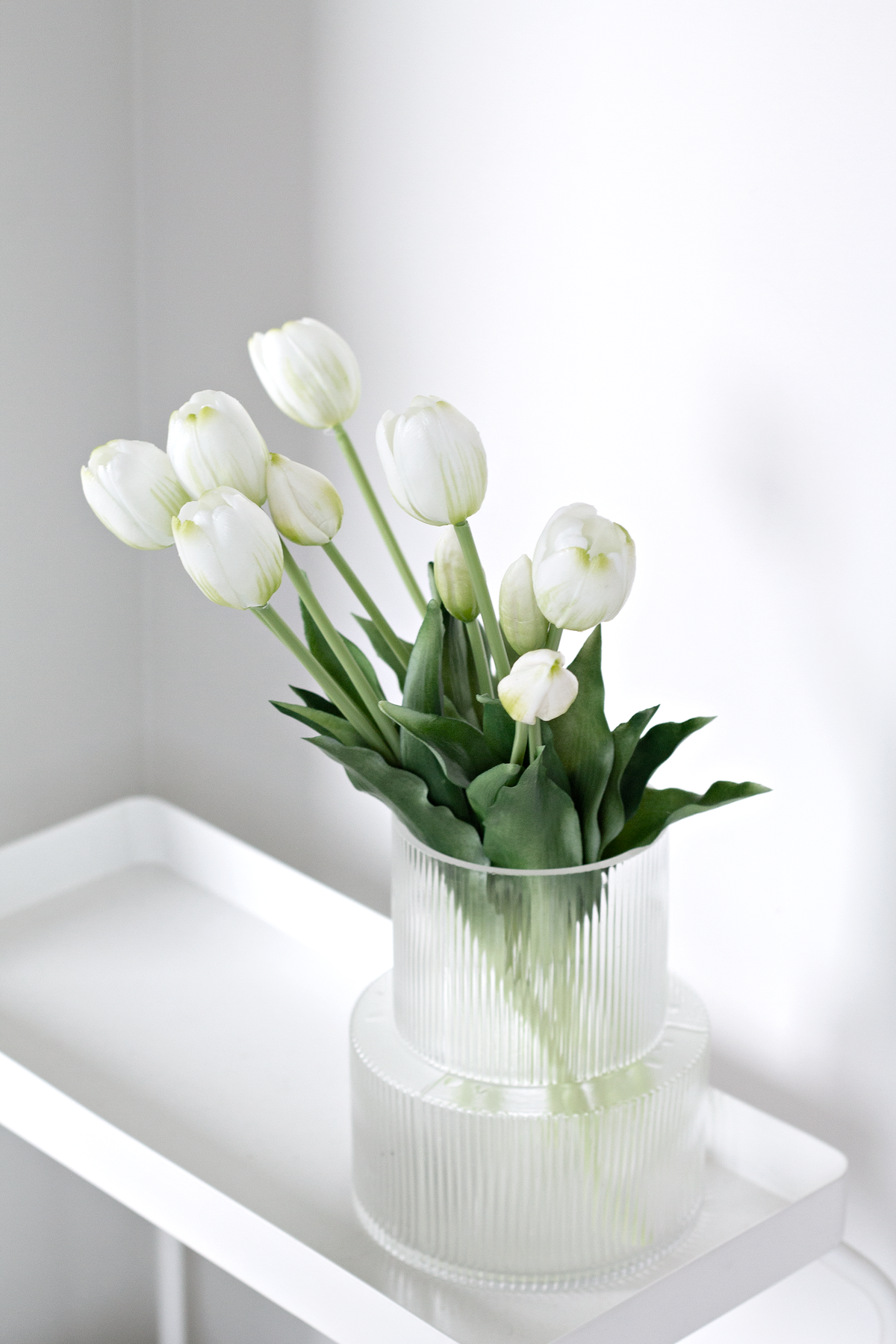 White faux tulips in a ribbed glass vase on a white side table