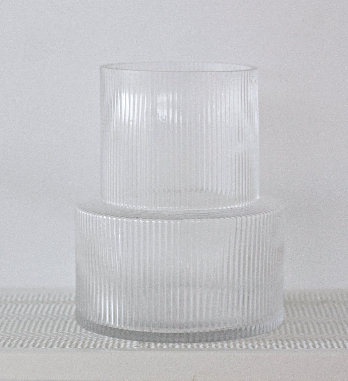 Clear ribbed vase shown straight on atop a woven placemat, fluting catching the light